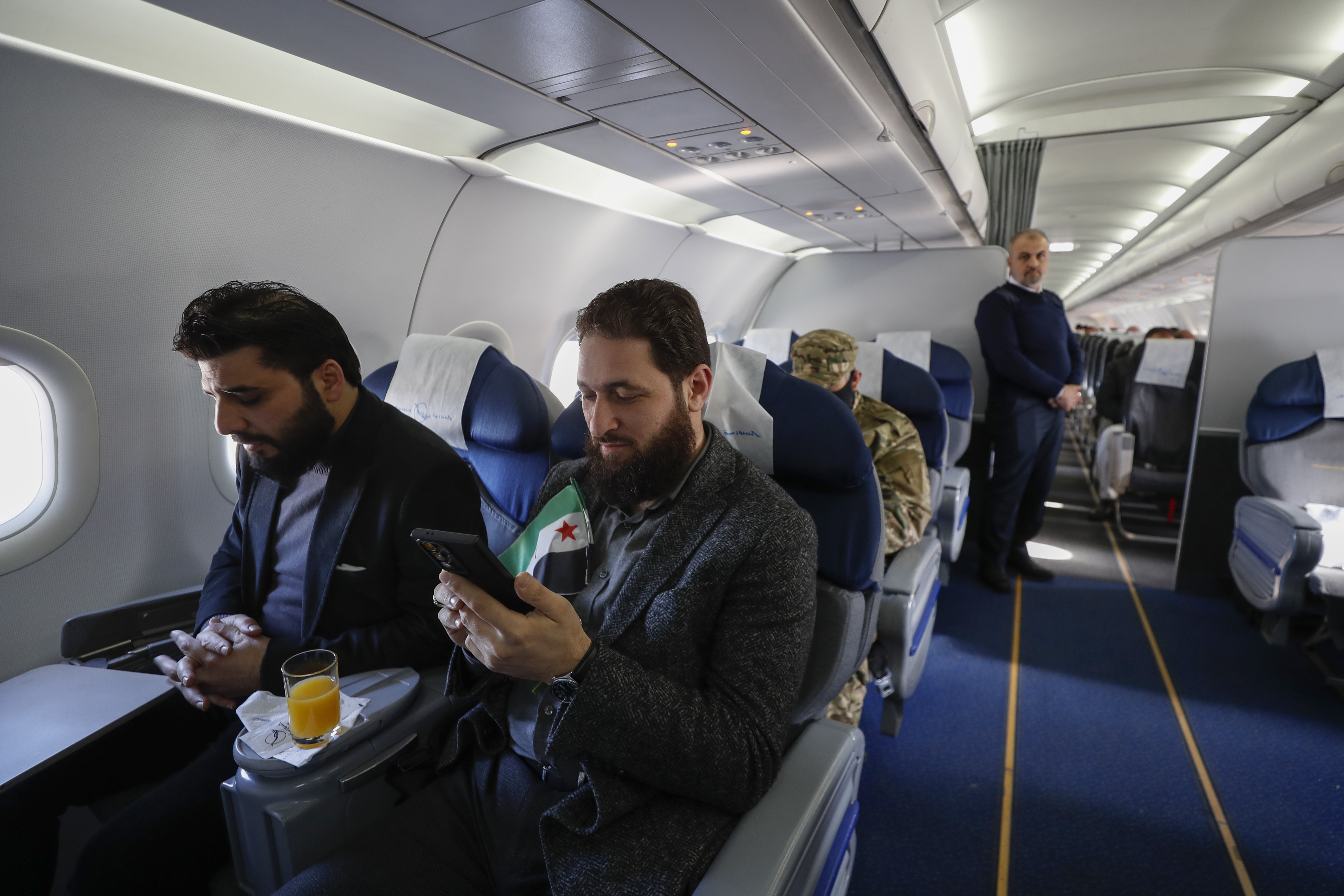 A man with a Syrian "revolutionary" flag sits inside a Syrian Air airplane ahead of take-off as the airport reopens for internal flights in Damascus, Syria, Wednesday, Dec. 18, 2024. (AP Photo/Omar Sanadiki)