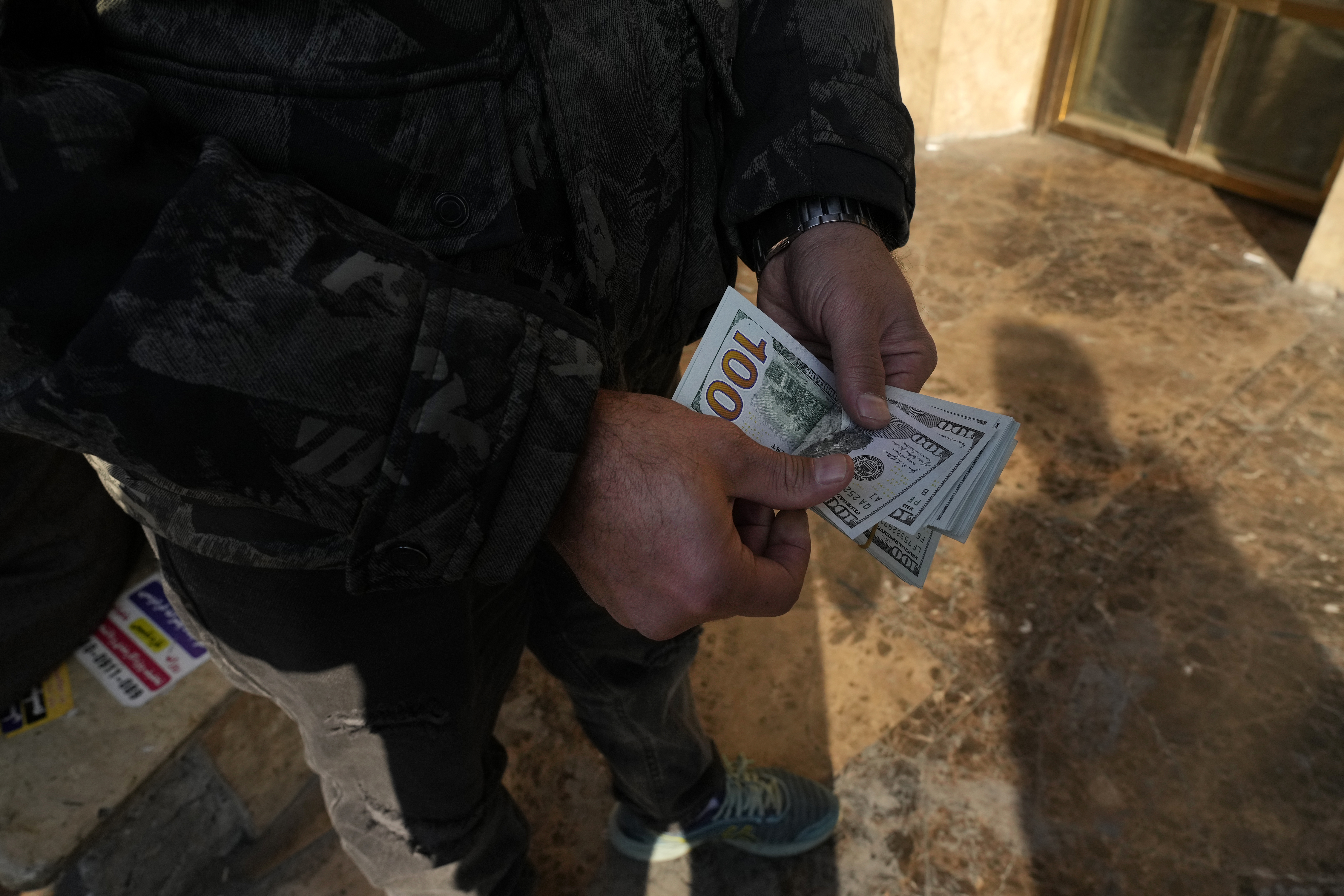 A man poses for a photo without showing his face as he counts U.S. dollars at Ferdowsi street, Tehran's go-to venue for foreign currency exchange, in downtown Tehran, Iran, Wednesday, Dec. 18, 2024. (AP Photo/Vahid Salemi)