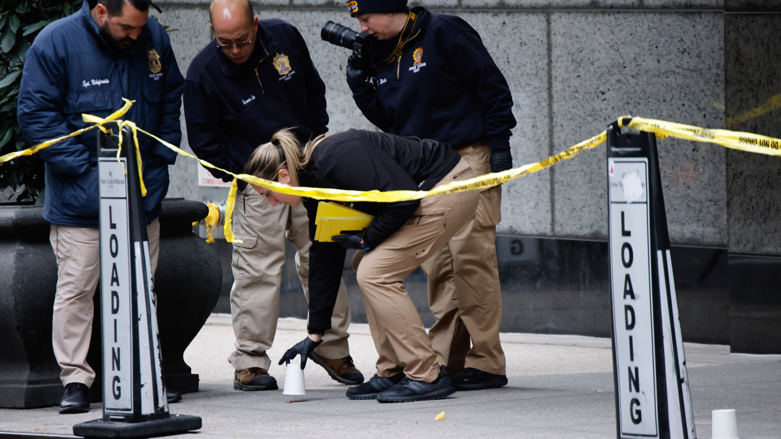 Members of the New York police crime scene unit pick up cups marking the spots where bullets lie as they investigate the scene outside the Hilton Hotel in midtown Manhattan where Brian Thompson, the CEO of UnitedHealthcare, was fatally shot Wednesday, Dec. 4, 2024, in New York. (AP Photo/Stefan Jeremiah)