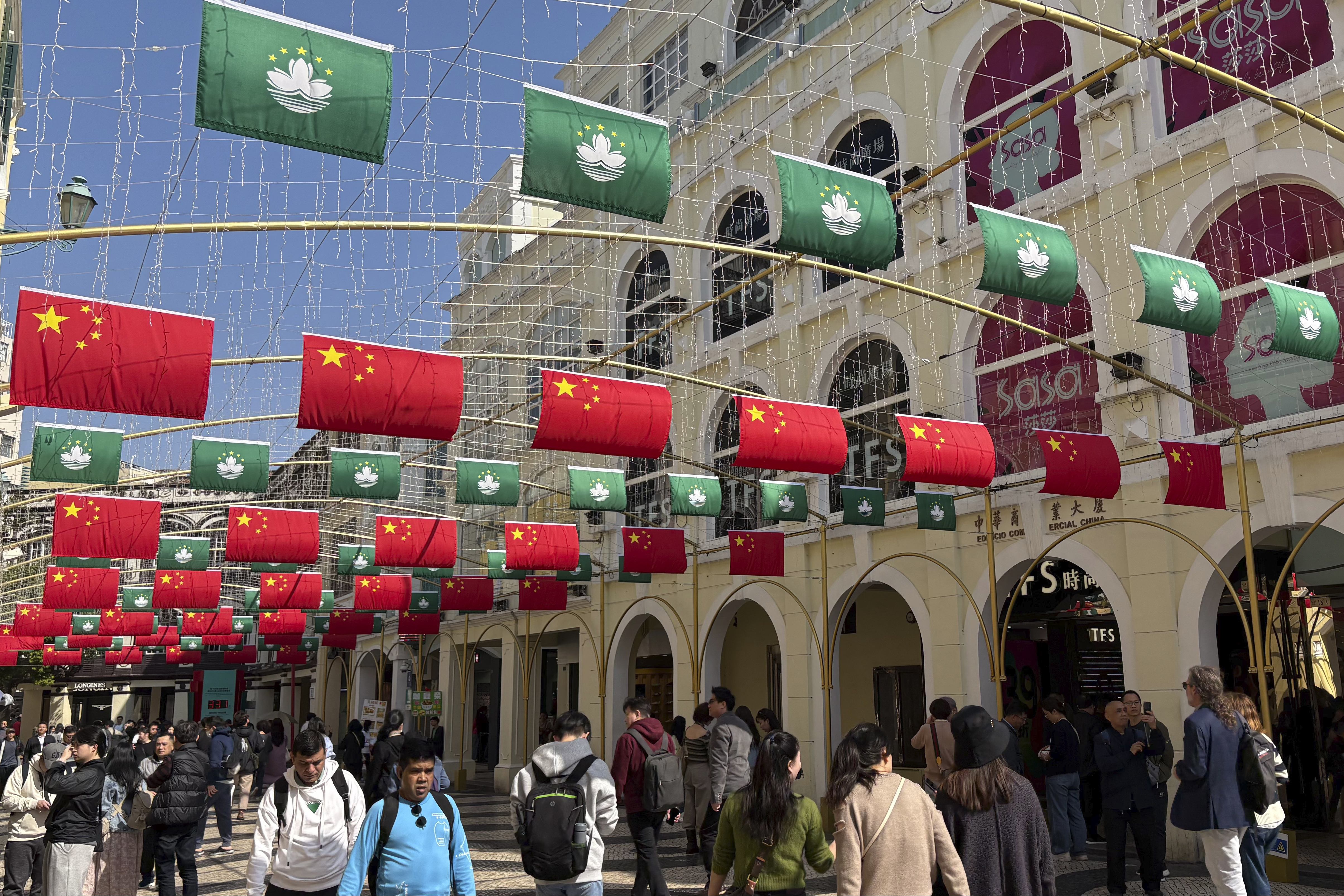 Tourists walk past a street decorated with Chinese national flags and Macao regional flags in Macao on Dec. 13, 2024. (AP Photo/Kanis Leung)