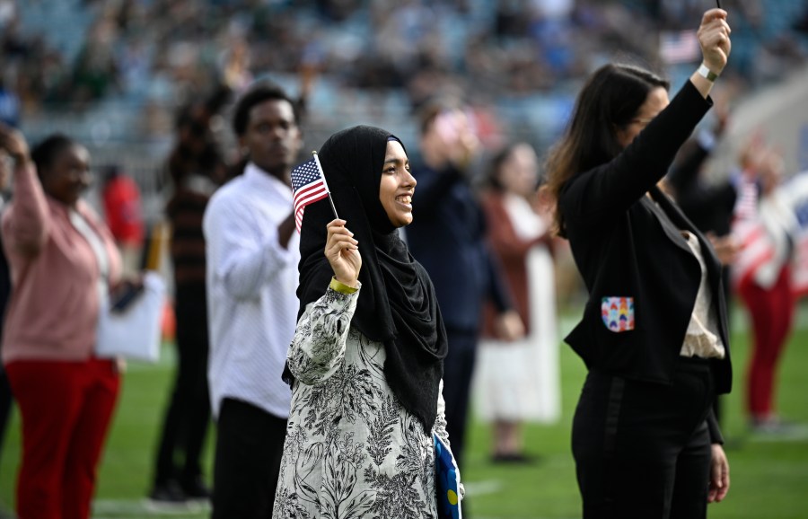 FILE - New United States citizens wave American flags during a naturalization ceremony during halftime at an NFL football game between the Jacksonville Jaguars and the New York Jets, Dec. 15, 2024, in Jacksonville, Fla. (AP Photo/Phelan M. Ebenhack, File)