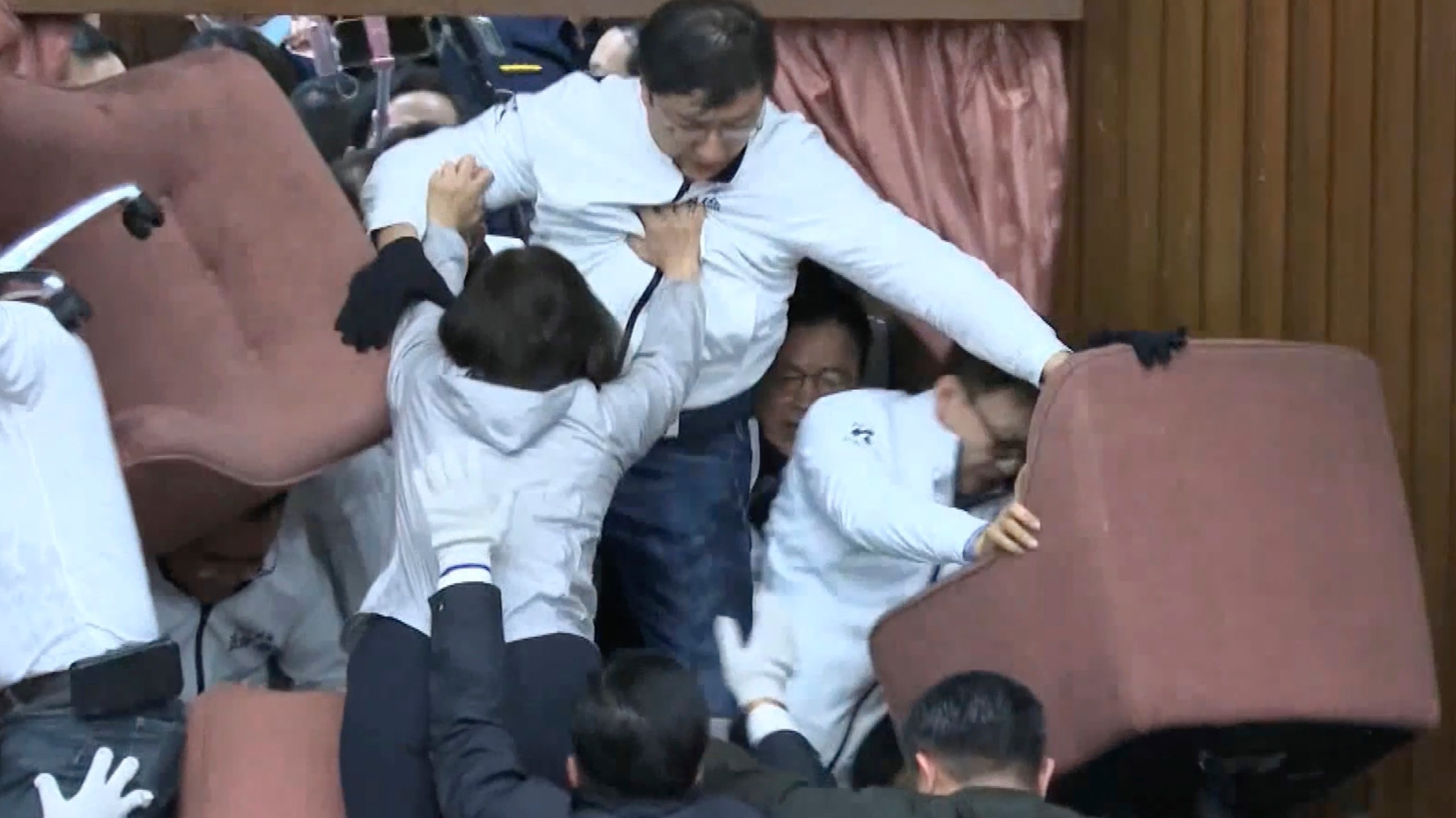 In this image made from video by Taiwan's EBC, lawmakers from the Democratic Progressive Party use chairs to block the entrance as members of the Nationalist Party, or Kuomintang, try to break into the Legislature in Taipei, Taiwan on Friday, Dec 20, 2024. (EBC via AP )