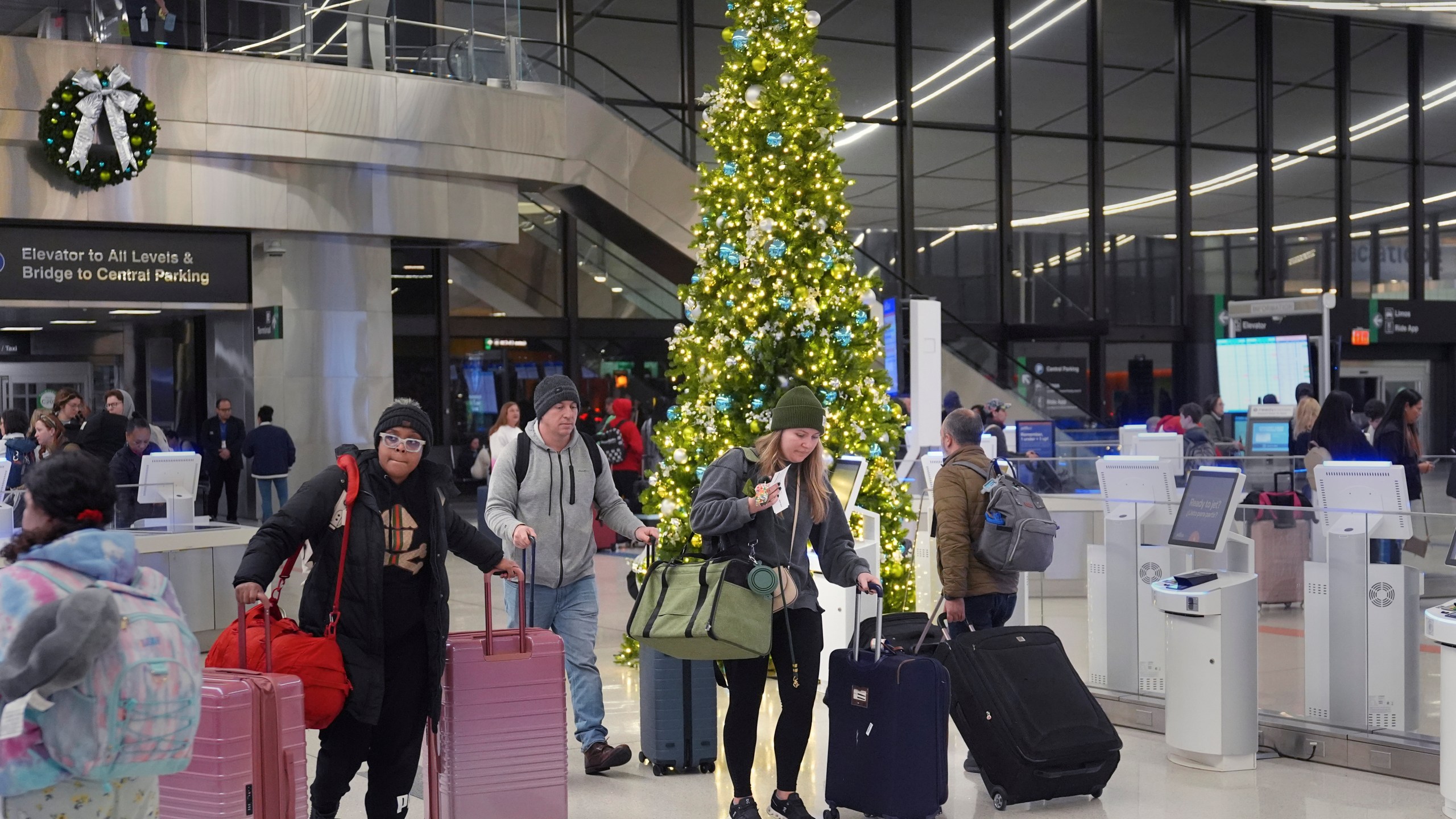 Holiday travelers pass a Christmas tree at Logan Airport, Friday, Dec. 20, 2024, in Boston. (AP Photo/Charles Krupa)