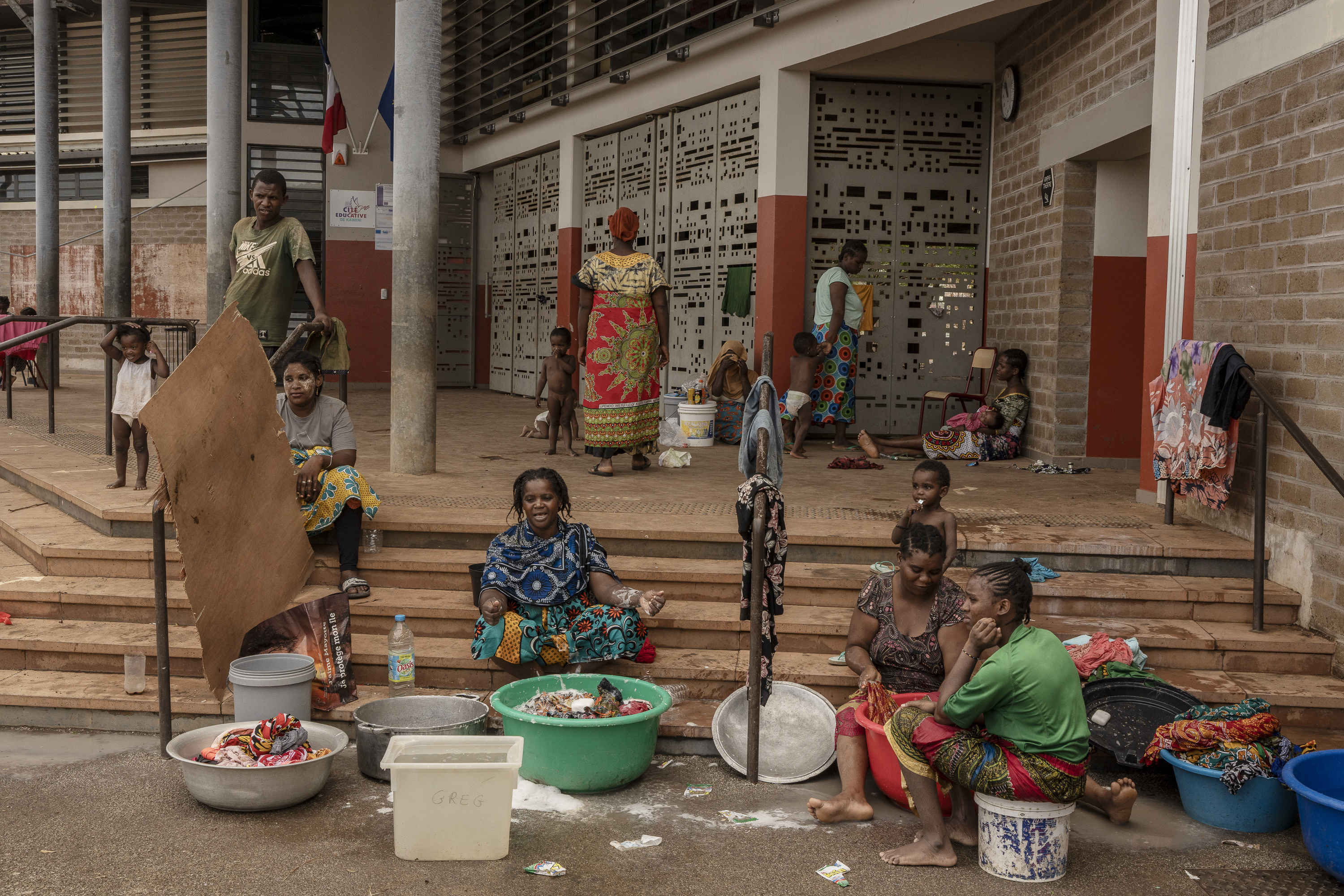 Women wash clothes after a short rain filled their pots with water, at the Lycée des Lumières where they found shelter after losing their homes, in Mamoudzou, Mayotte, Thursday, Dec. 19, 2024 . (AP Photo/Adrienne Surprenant)