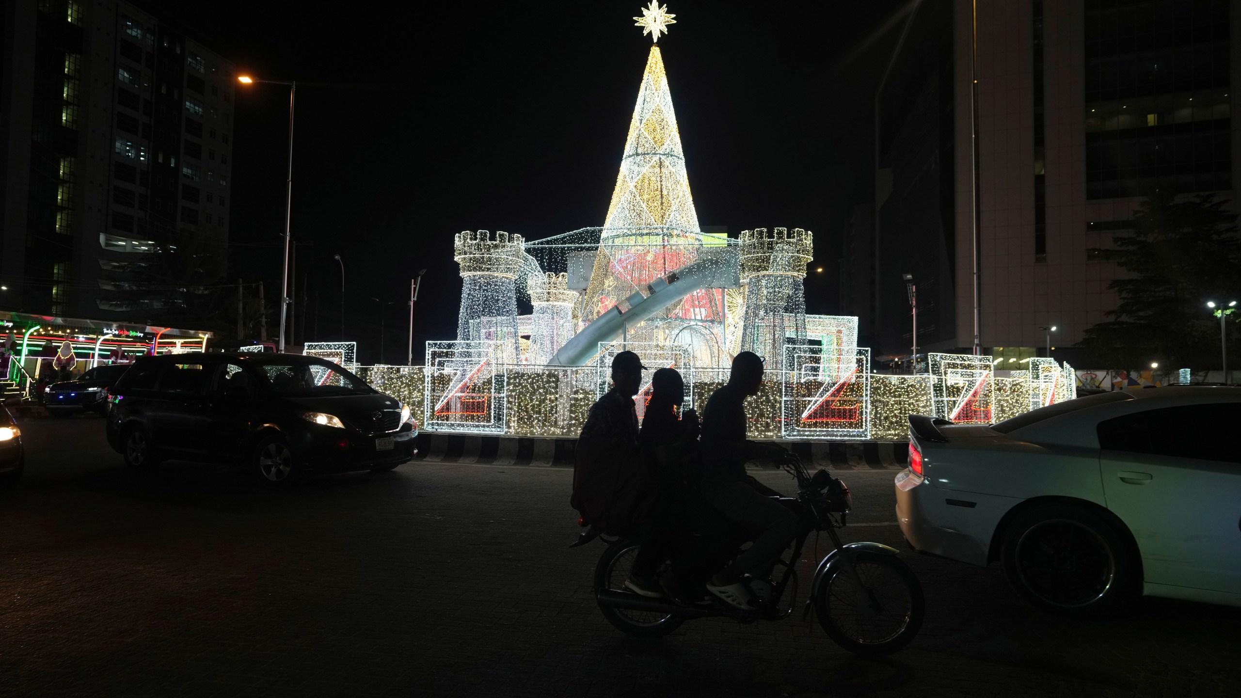 A man rides a motorcycle taxi past Christmas decorations on a street in Lagos, Nigeria, Friday, Dec. 20, 2024. (AP Photo/Sunday Alamba)