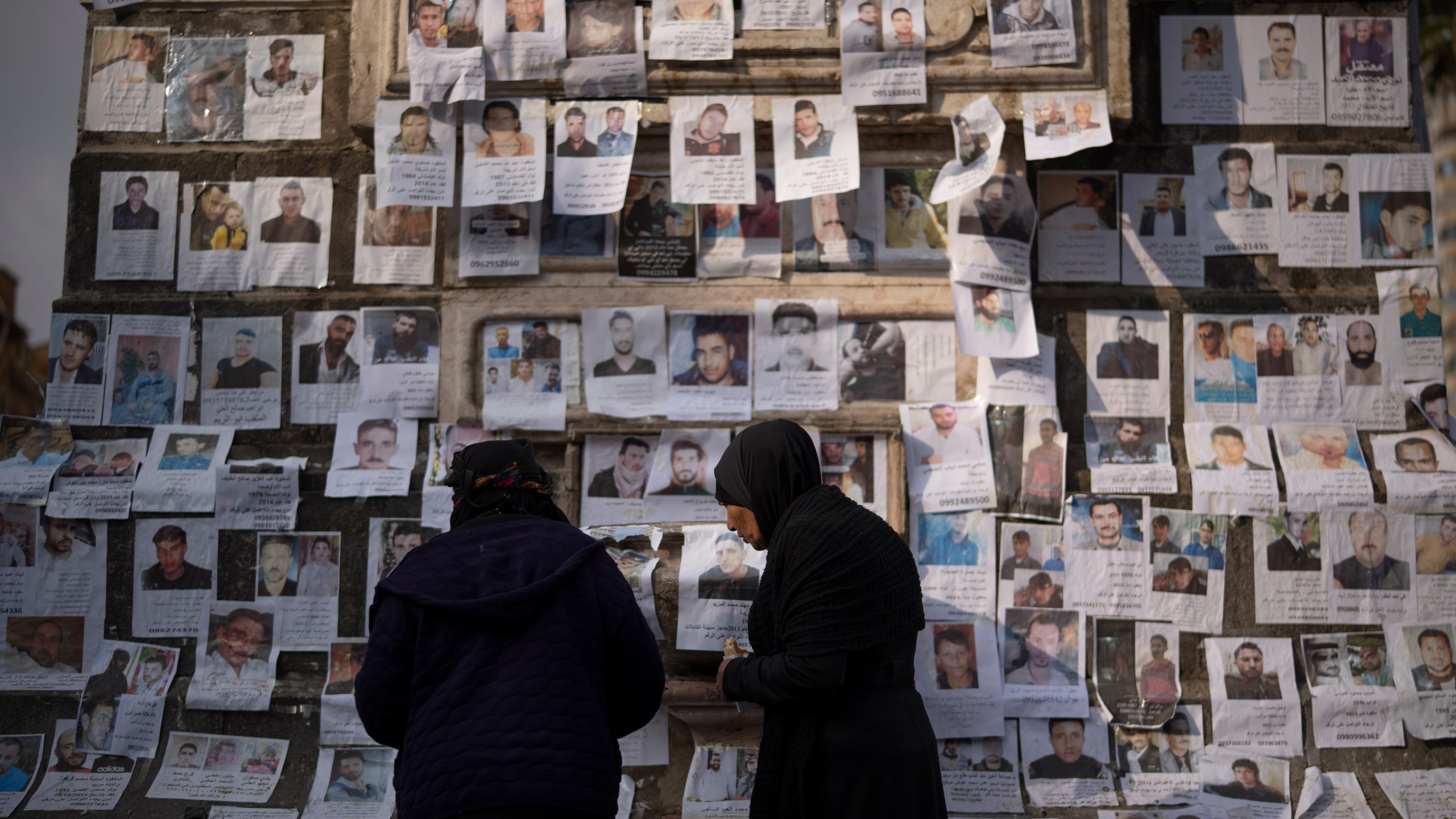 Women look at photos of people reported to be missing by members of ousted Syrian President Bashar Assad's army, or a pro-government militia, in the Marjeh square in Damascus, Syria, Sunday, Dec. 22, 2024. (AP Photo/Leo Correa)