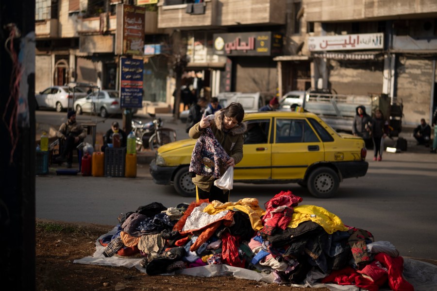 A women looks at second hand clothes displayed on a street for sale near an Alawite neighbourhood, in Homs, Syria, Thursday, Dec. 26, 2024. (AP Photo/Leo Correa)