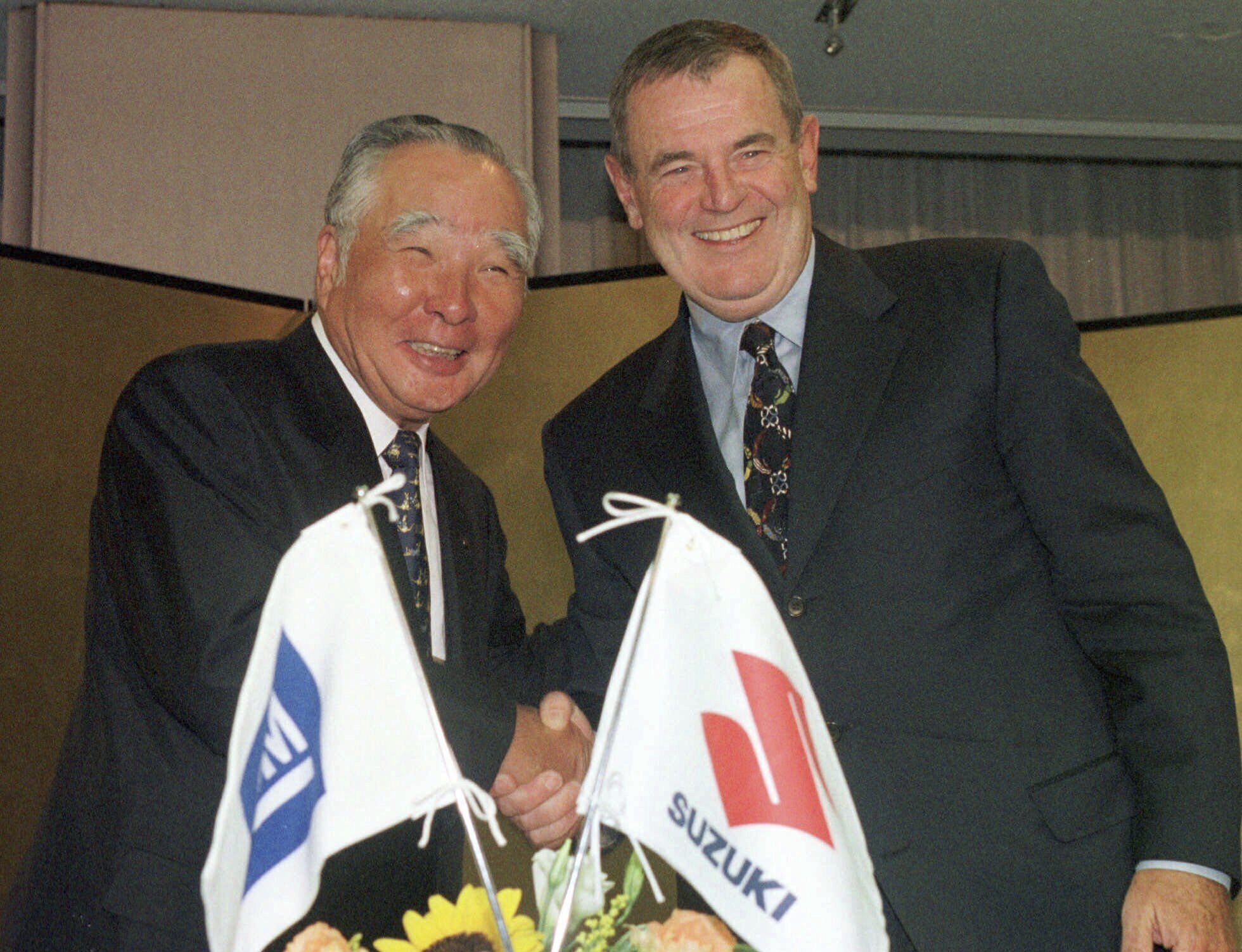 FILE - General Motors Chairman John F. Smith, left, and Osamu Suzuki, president and CEO of Suzuki Motor Corp., smile after announcing the two automakers' agreement to increase coordination of their global manufacturing operations in Tokyo, Sept. 16, 1998. (AP Photo/Katsumi Kasahara, File)