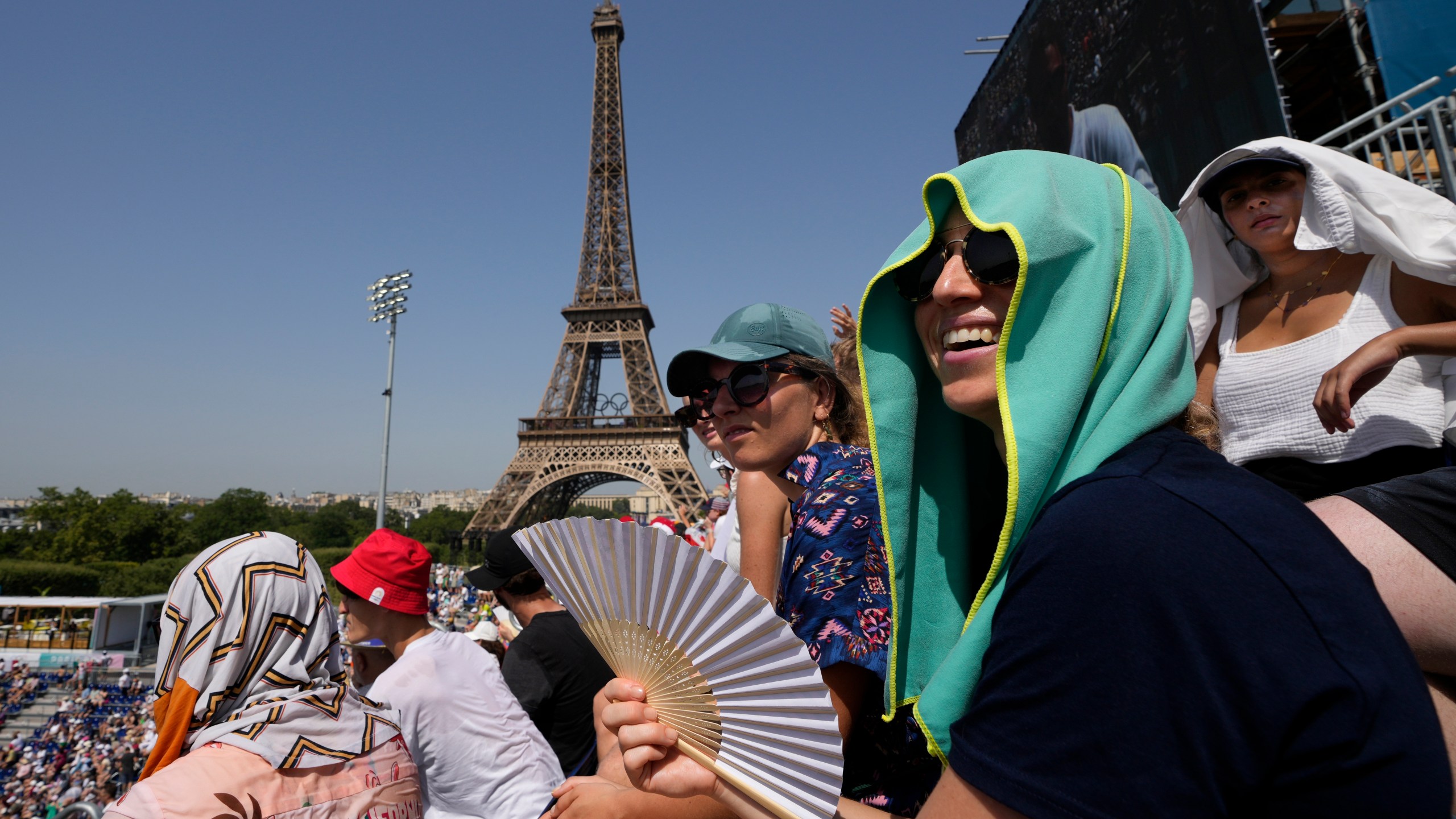 FILE - Stephanie Touissaint, foreground, uses a fan to keep cool in the sweltering heat at Eiffel Tower Stadium during a beach volleyball match between Cuba and Brazil at the 2024 Summer Olympics, July 30, 2024, in Paris, France. (AP Photo/Robert F. Bukaty, File)