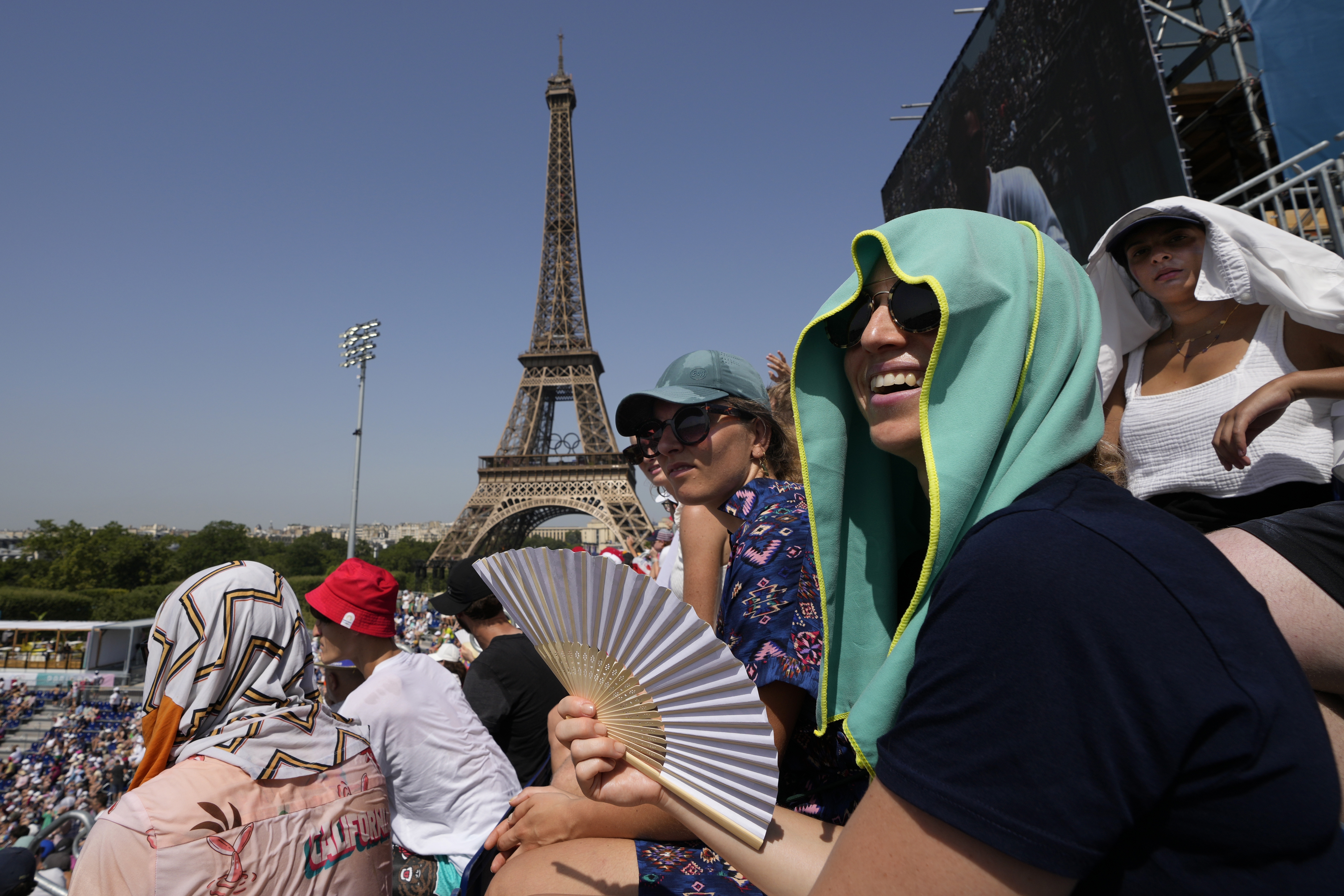 FILE - Stephanie Touissaint, foreground, uses a fan to keep cool in the sweltering heat at Eiffel Tower Stadium during a beach volleyball match between Cuba and Brazil at the 2024 Summer Olympics, July 30, 2024, in Paris, France. (AP Photo/Robert F. Bukaty, File)