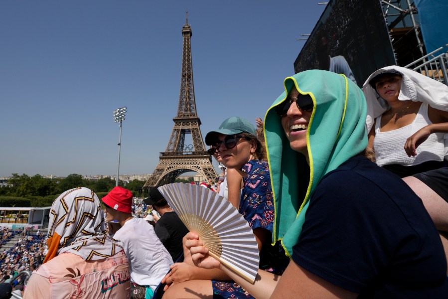 FILE - Stephanie Touissaint, foreground, uses a fan to keep cool in the sweltering heat at Eiffel Tower Stadium during a beach volleyball match between Cuba and Brazil at the 2024 Summer Olympics, July 30, 2024, in Paris, France. (AP Photo/Robert F. Bukaty, File)