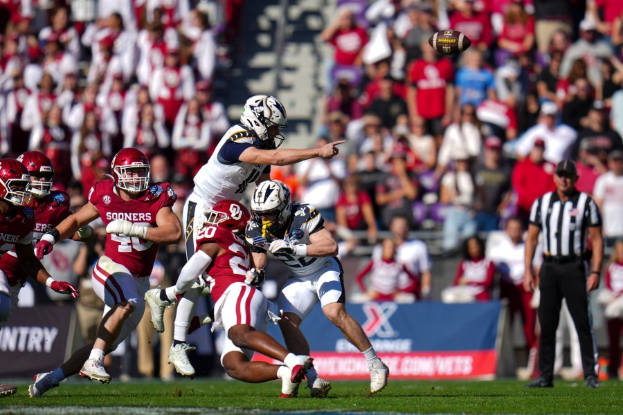 Navy quarterback Blake Horvath, top left, takes a hit from Oklahoma linebacker Lewis Carter (20) while attempting a pass during the first half of the Armed Forces Bowl NCAA college football game, Friday, Dec. 27, 2024, in Fort Worth, Texas. (AP Photo/Julio Cortez)