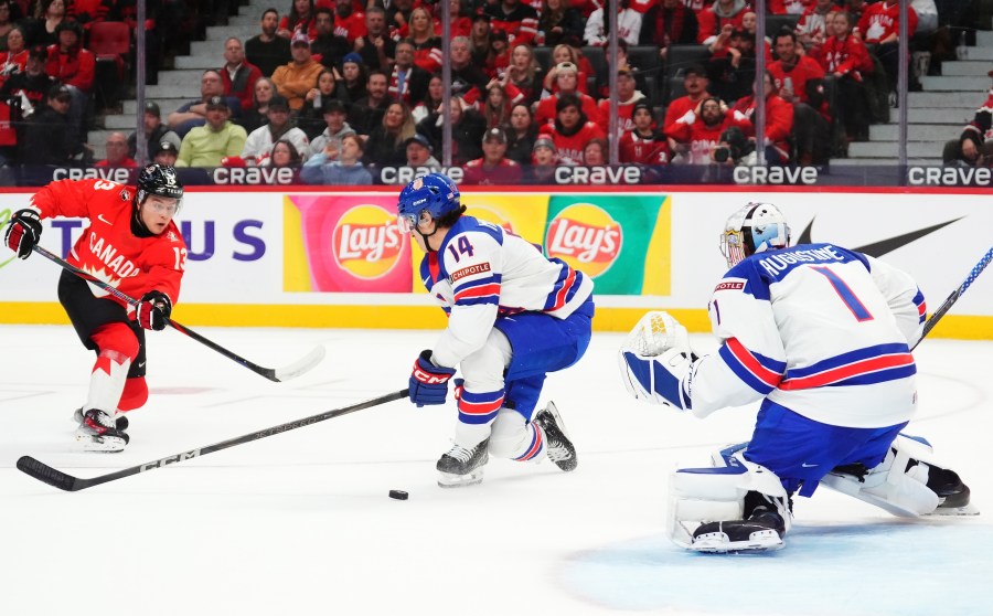 Canada's Luca Pinelli (13) shoots against United States goaltender Trey Augustine (1) as United States' Aram Minnetian (14) defends during second-period IIHF World Junior Hockey Championship tournament game action in Ottawa, Ontario, Tuesday, Dec. 31, 2024. (Sean Kilpatrick/The Canadian Press via AP)