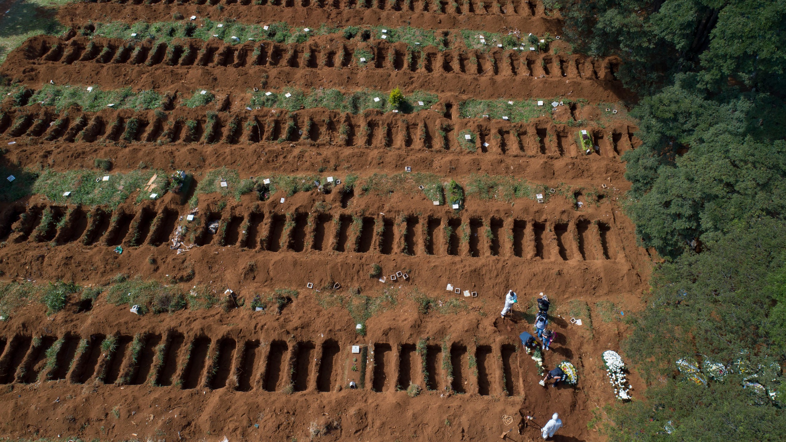 FILE - Cemetery workers in protective gear bury a person alongside rows of freshly dug graves at the Vila Formosa cemetery in Sao Paulo, Brazil, April 1, 2020. (AP Photo/Andre Penner, File)