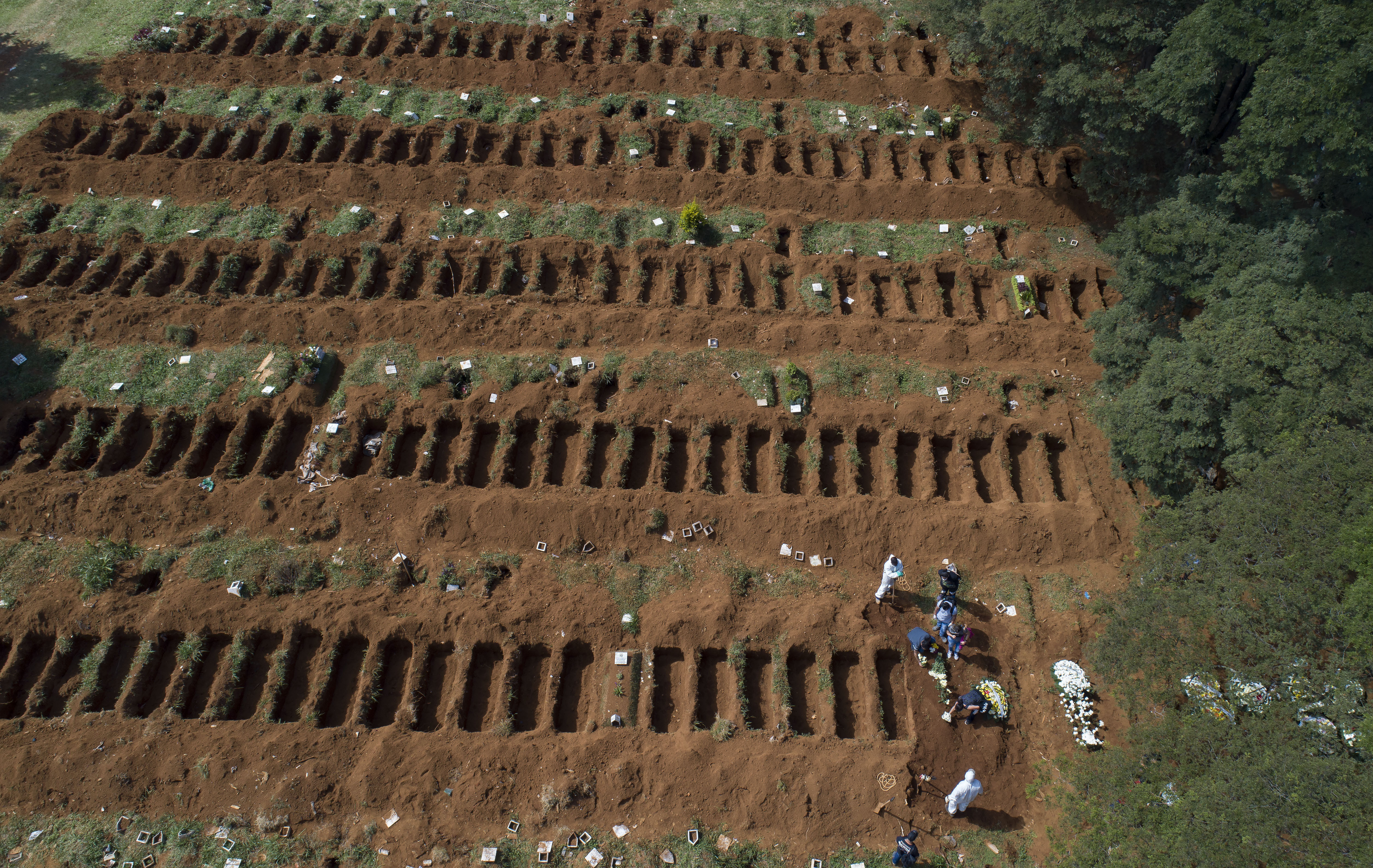 FILE - Cemetery workers in protective gear bury a person alongside rows of freshly dug graves at the Vila Formosa cemetery in Sao Paulo, Brazil, April 1, 2020. (AP Photo/Andre Penner, File)