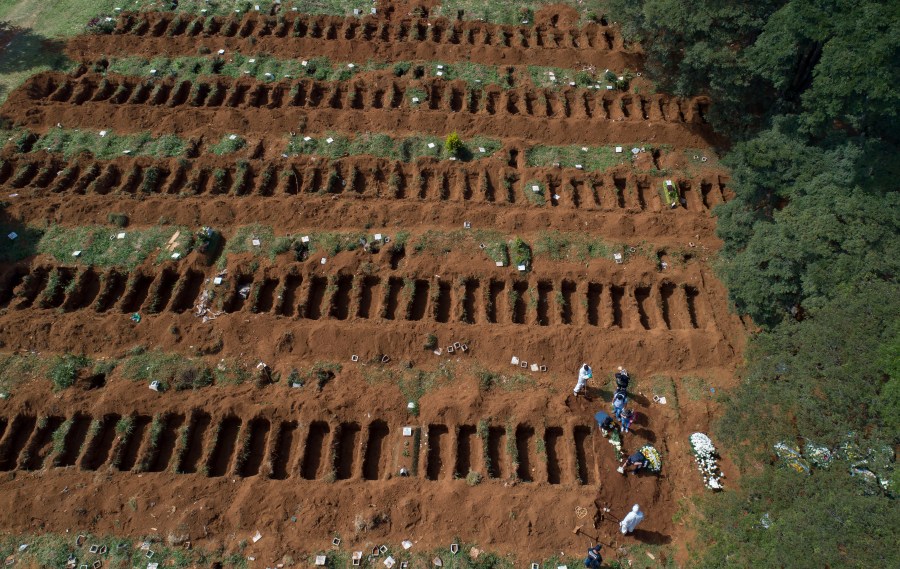 FILE - Cemetery workers in protective gear bury a person alongside rows of freshly dug graves at the Vila Formosa cemetery in Sao Paulo, Brazil, April 1, 2020. (AP Photo/Andre Penner, File)