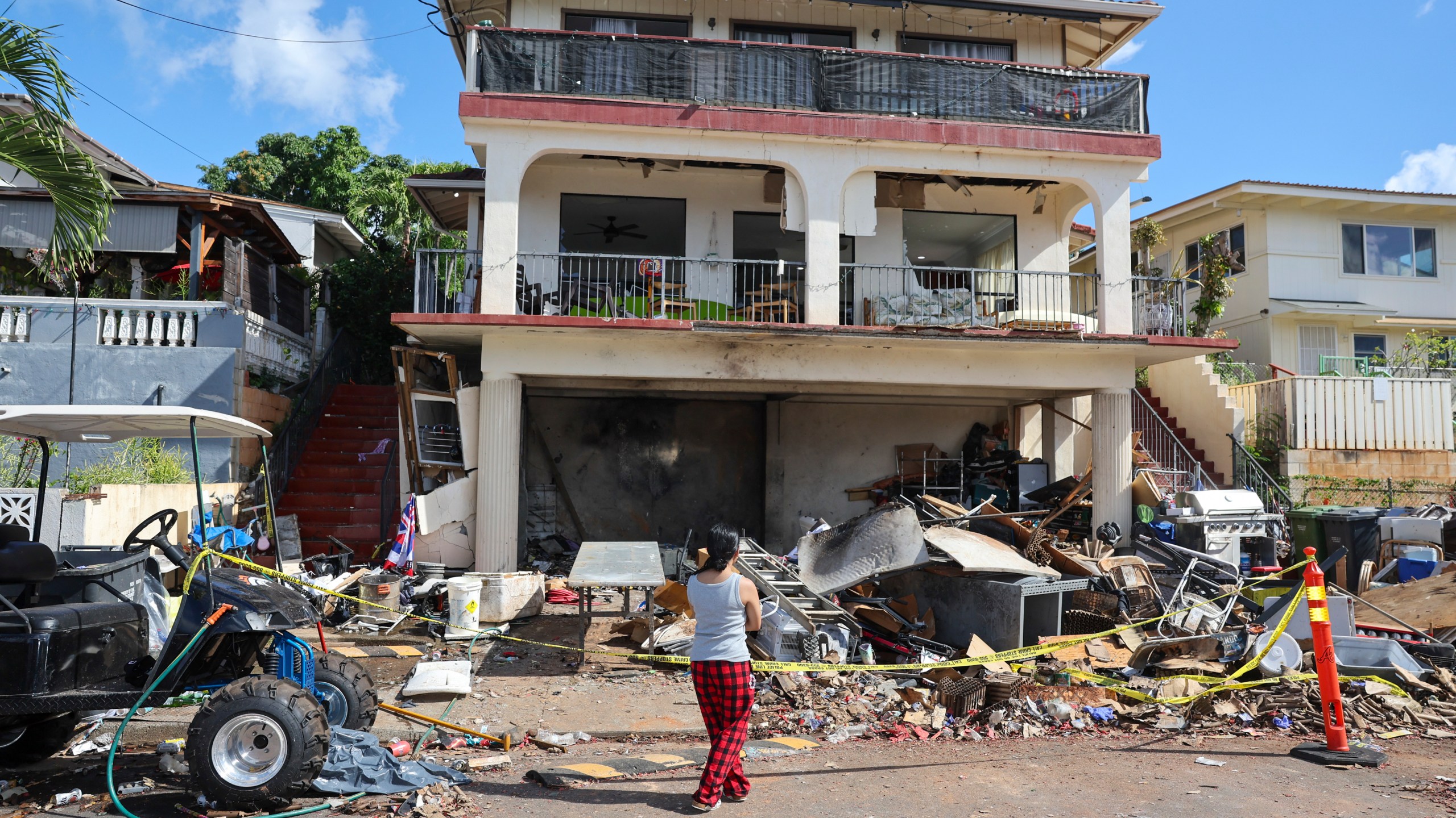 A woman stands in front of the home where a New Year's Eve fireworks explosion killed and injured people, Wednesday, Jan. 1, 2025, in Honolulu. (AP Photo/Marco Garcia)