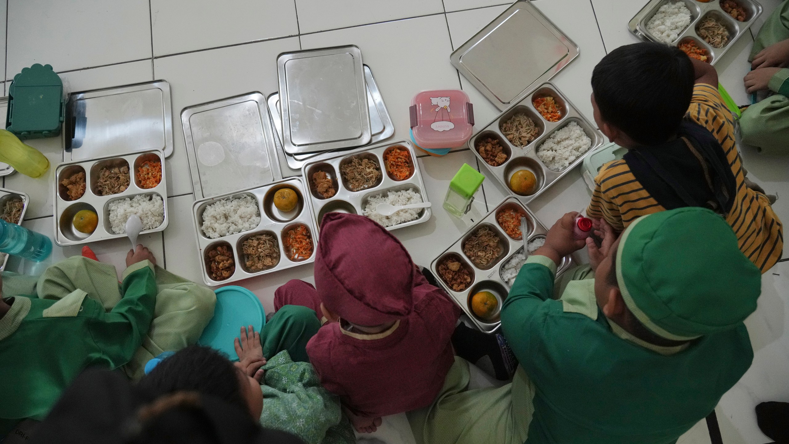 Students sit on the floor as they have their meals during the kick off of President Prabowo Subianto's ambitious free meal program to feed children and pregnant women nationwide despite critics saying that its required logistics could hurt Indonesia's state finances and economy at Early Childhood Education and Development in Jakarta, Indonesia, Monday, Jan. 6, 2025. (AP Photo/Achmad Ibrahim)