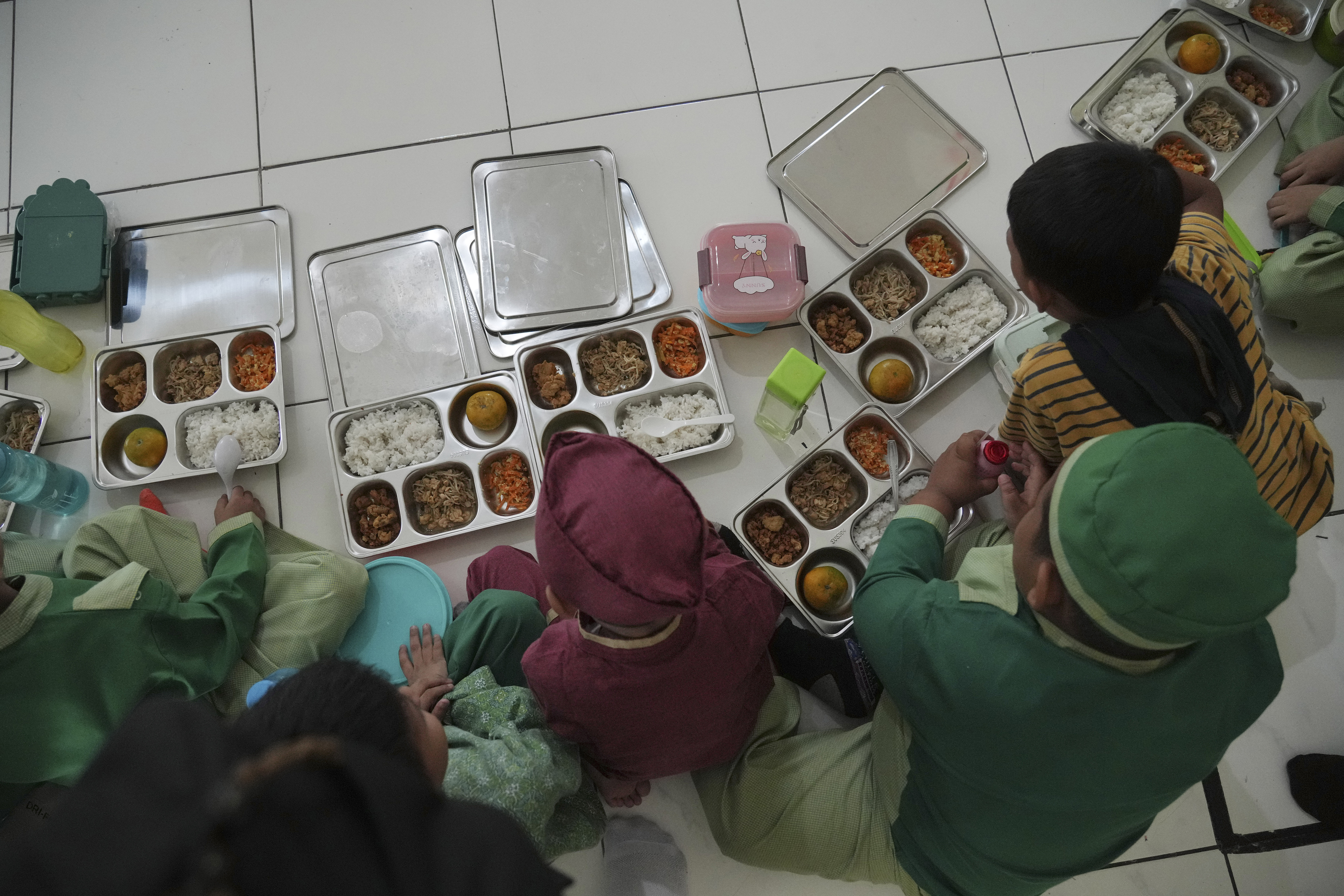 Students sit on the floor as they have their meals during the kick off of President Prabowo Subianto's ambitious free meal program to feed children and pregnant women nationwide despite critics saying that its required logistics could hurt Indonesia's state finances and economy at Early Childhood Education and Development in Jakarta, Indonesia, Monday, Jan. 6, 2025. (AP Photo/Achmad Ibrahim)