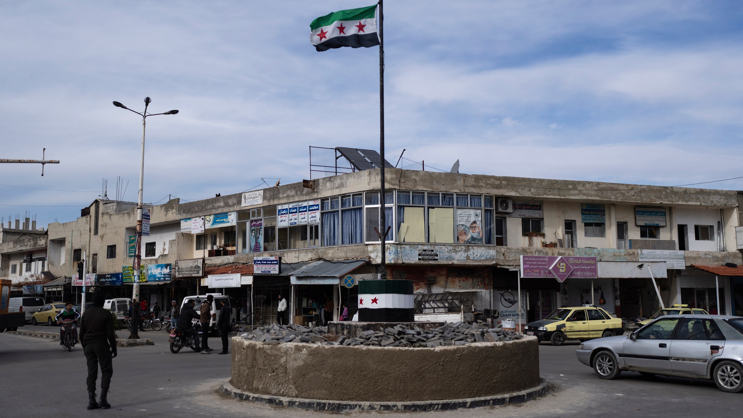 Cars drive past a roundabout hoisting the new Syrian flag after the ousting of the Assad regime, in Salam City, formerly called Baath City after the ruling party, in Quneitra, Syria, Sunday, Jan. 5, 2025. (AP Photo/Mosa'ab Elshamy)