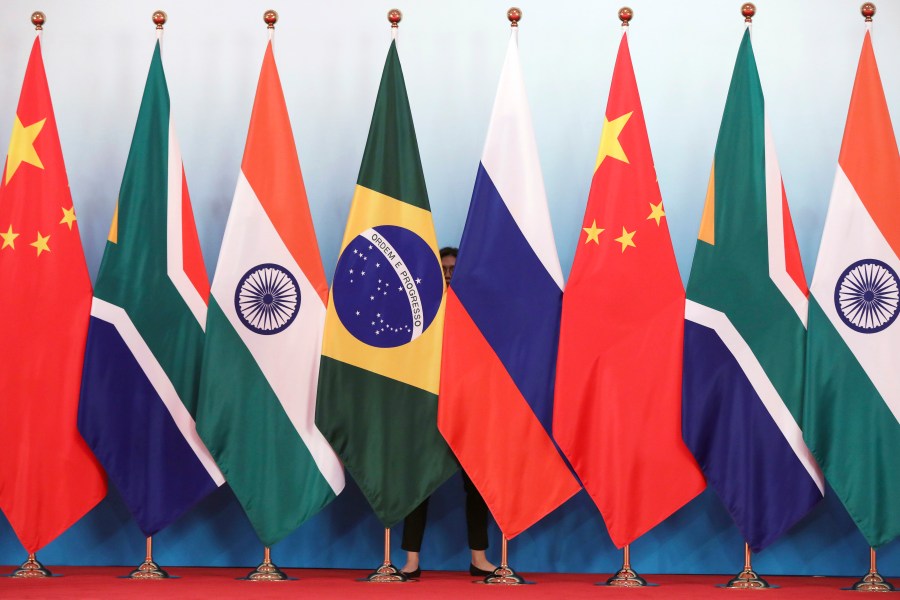 FILE - Staff worker stands behinds national flags of Brazil, Russia, China, South Africa and India to tidy the flags ahead of a group photo during the BRICS Summit at the Xiamen International Conference and Exhibition Center in Xiamen, southeastern China's Fujian Province, Monday, Sept. 4, 2017. (Wu Hong/Pool Photo via AP, File)