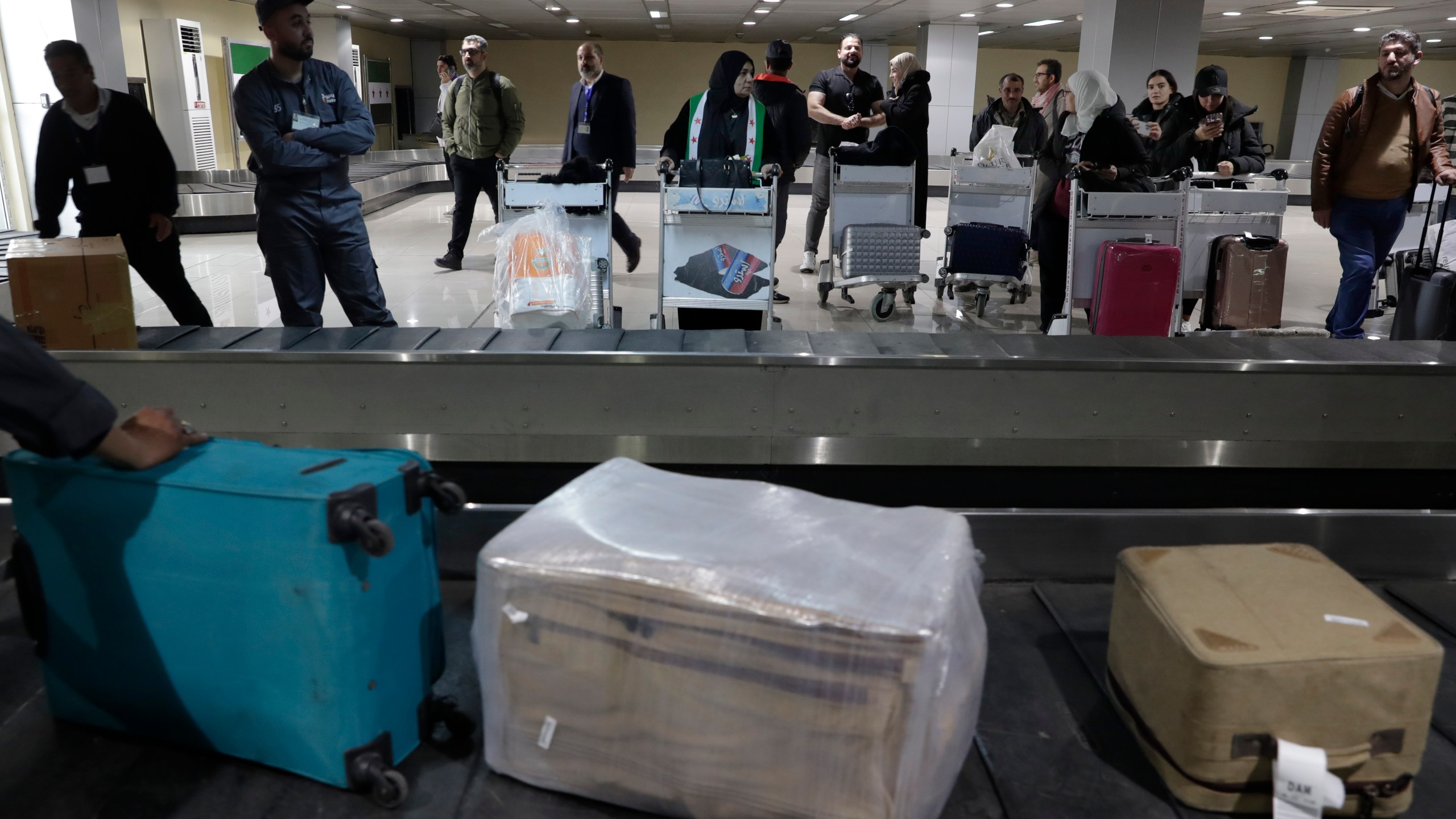 Passengers who arrived at a first international commercial flight since the fall of former Syrian President Bashar Assad, wait to receive their luggages at the arrival terminal of Damascus international airport, in Damascus, Syria, Tuesday, Jan. 7, 2025. (AP Photo/Omar Sanadiki)