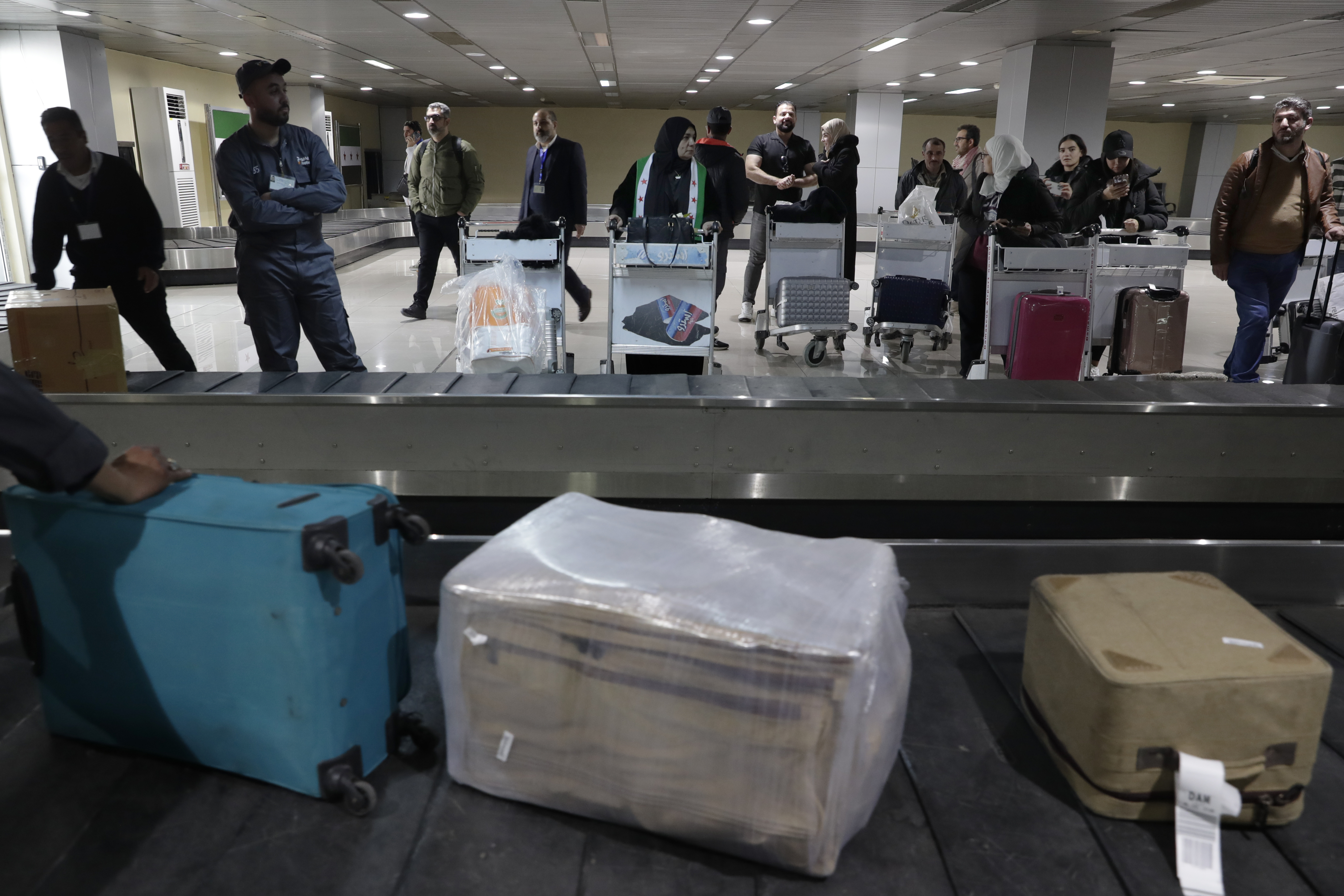 Passengers who arrived at a first international commercial flight since the fall of former Syrian President Bashar Assad, wait to receive their luggages at the arrival terminal of Damascus international airport, in Damascus, Syria, Tuesday, Jan. 7, 2025. (AP Photo/Omar Sanadiki)