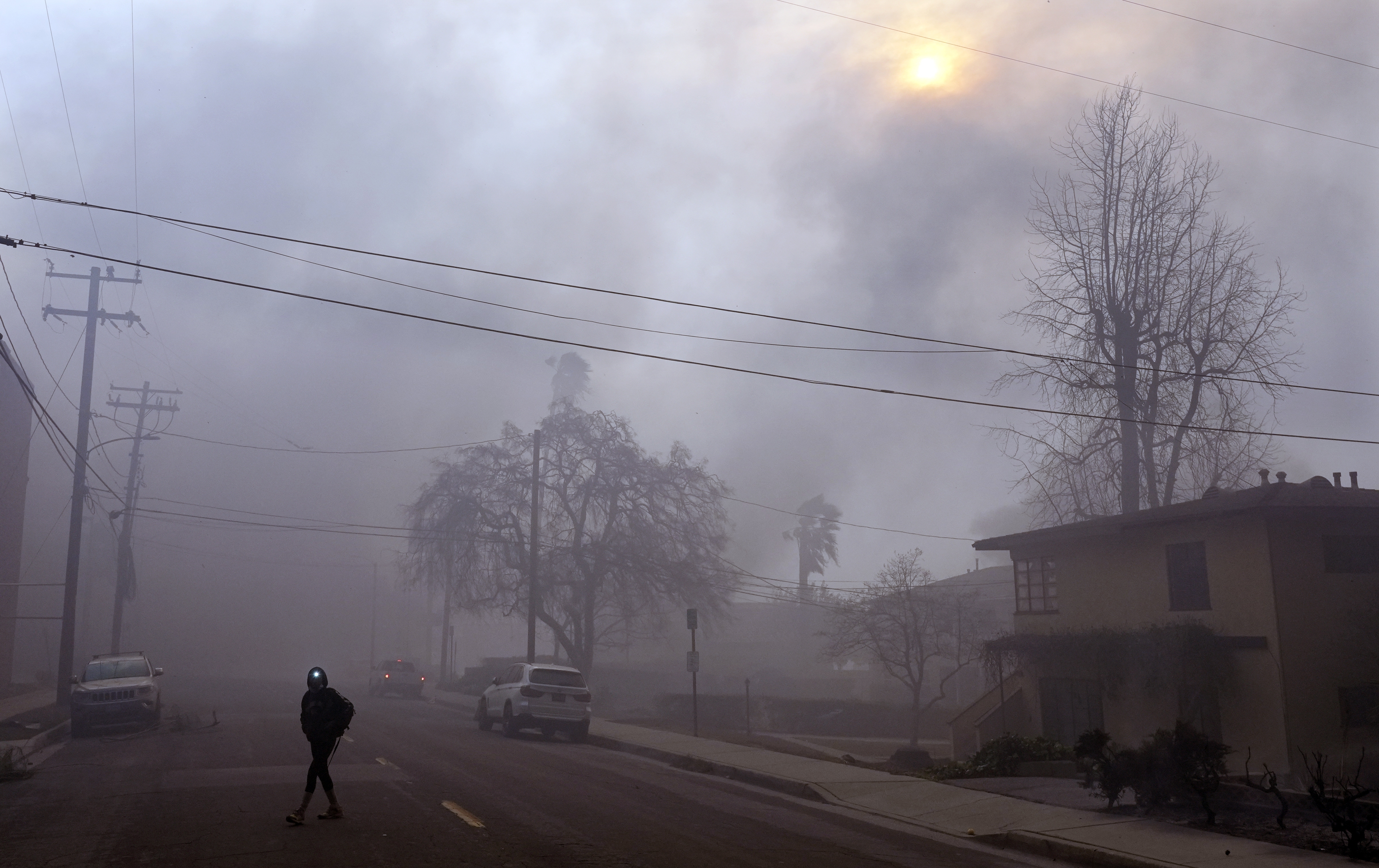 A pedestrian uses a flashlight to make his way down a smoke-filled street during wildfires in the Altadena section of Pasadena, Calif., Wednesday, Jan. 8, 2025. (AP Photo/Chris Pizzello)