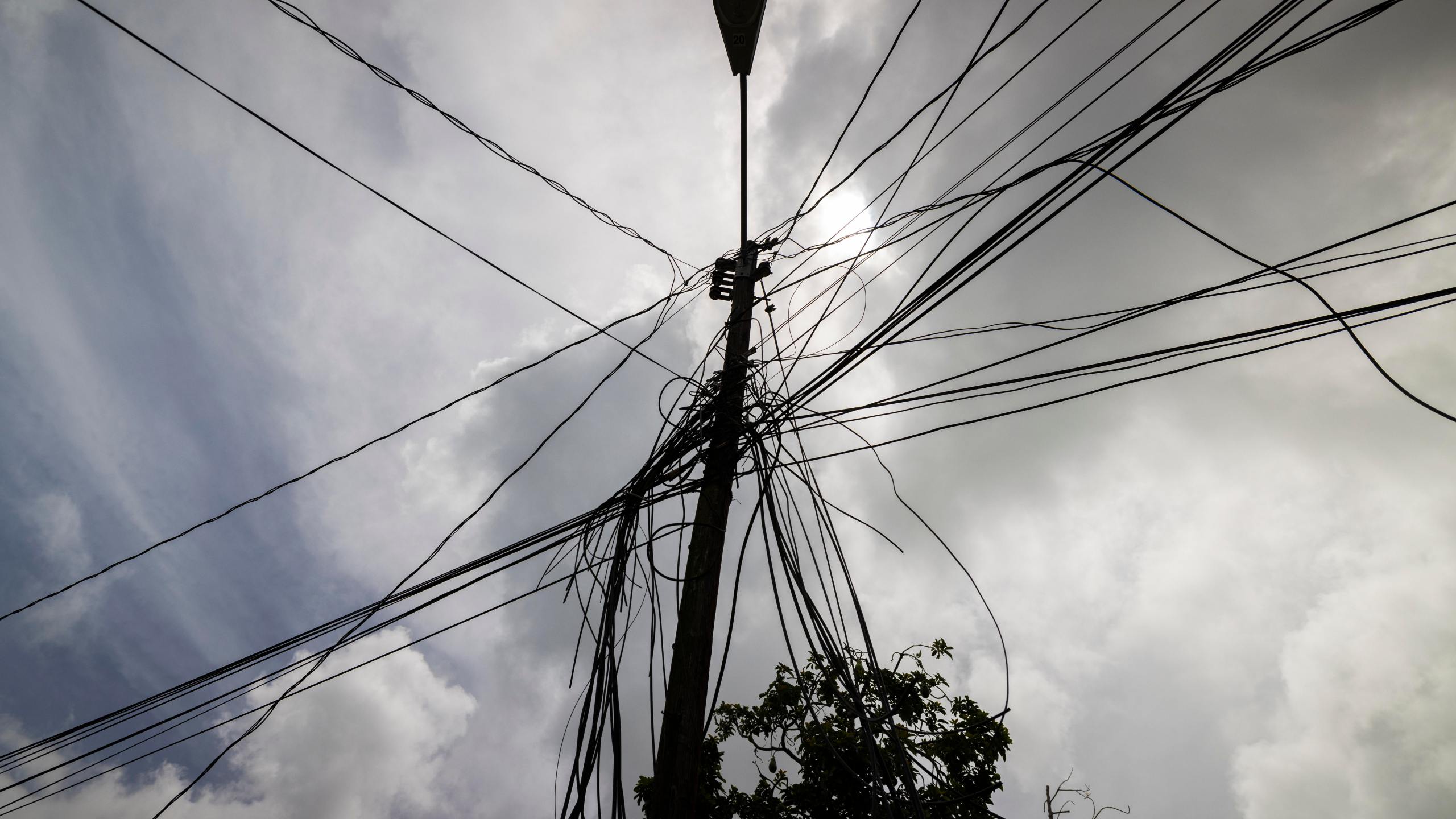 FILE - A utility pole with loose cables towers over a home in Loiza, Puerto Rico, Sept. 15, 2022. (AP Photo/Alejandro Granadillo, File)