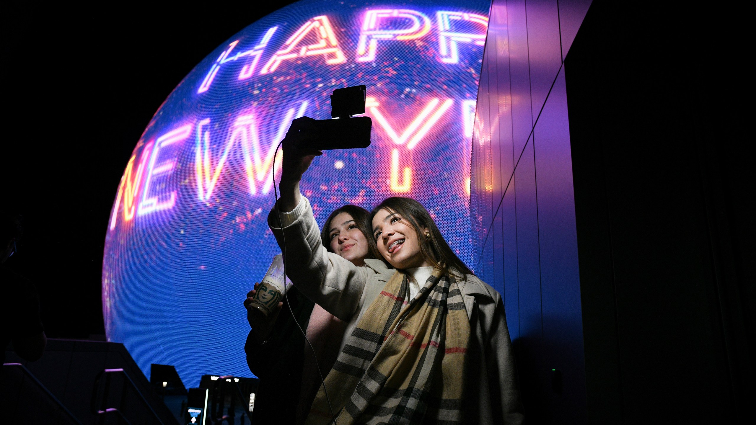 Paulina Mojica, left, and Isabelle Mojica take a selfie as the Sphere displays a Happy New Year message Tuesday, December 31, 2024, in Las Vegas. (Sam Morris/Las Vegas Review-Journal via AP)