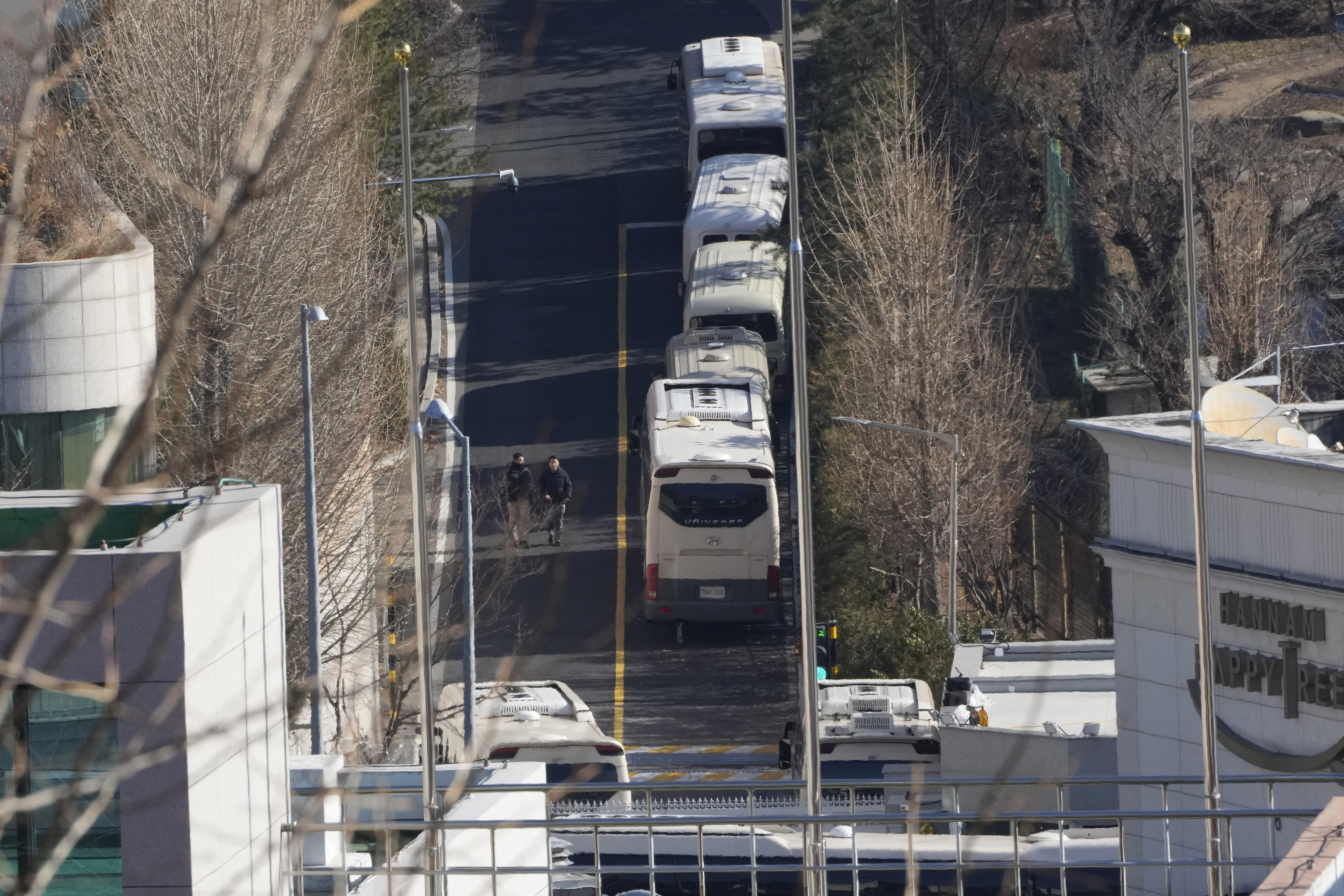 Security personnel walk on a road lined up with buses blocking the entrance gate of impeached South Korean President Yoon Suk Yeol's residence in Seoul, South Korea, Friday, Jan. 10, 2025. (AP Photo/Ahn Young-joon)