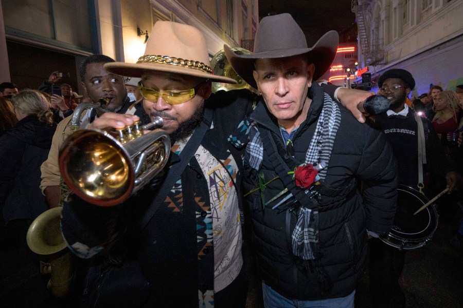 Amir "Tubad" Gray, left, leads Tubad and the Kings of NOLA Brass Band and artist Roberto Marquez, right, in New Orleans, Saturday, Jan. 4, 2025, as they memorialize the victims of the New Year's Day deadly truck attack and shooting. Marquez organized the parade and vigil and designed a memorial for the victims on Bourbon Street. (AP Photo/Matthew Hinton)