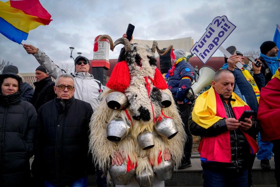 A person dressed in a costume made out of fur stands next to people waving flags and holding a banner that reads "Give us back the second round!" during a rally organized by the right wing Alliance for the Unity of Romanians (AUR), calling for free elections after Romania' s Constitutional Court annulled the first round of presidential elections last December, in Bucharest, Romania, Sunday, Jan. 12, 2025. (AP Photo/Vadim Ghirda)