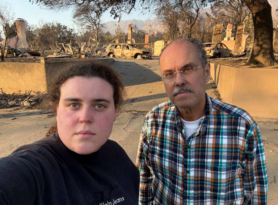 Vanessa Prata and her father, Aluizio Prata, pose for a self-portrait in Altadena, Calif., on Saturday, Jan. 11, 2025, with damage from the Eaton fire behind them. (Vanessa Prata via AP)