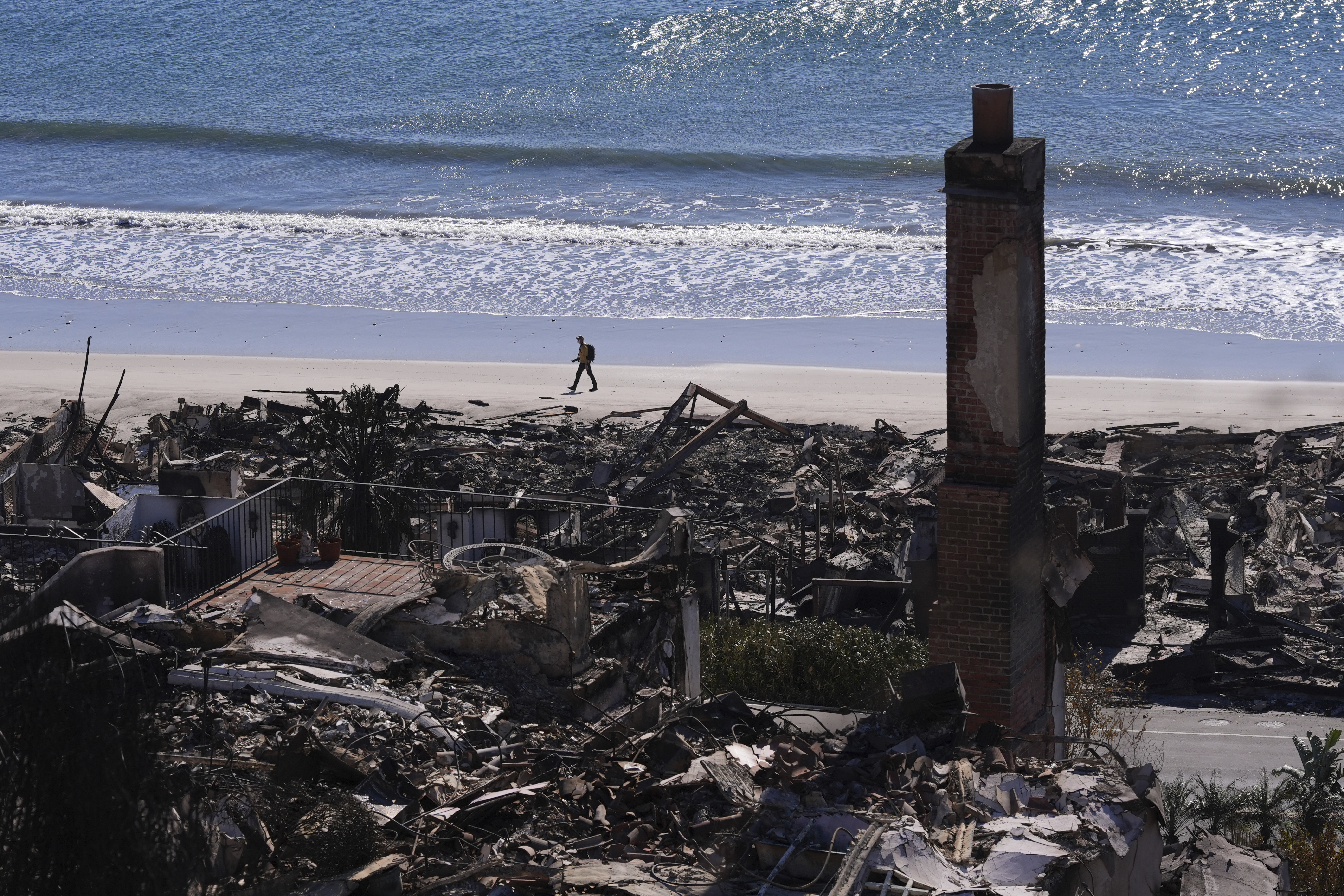 A person walks along a beach past homes destroyed by the Palisades Fire along the Pacific Coast Highway in Malibu, Calif., Sunday, Jan. 12, 2025. (AP Photo/Mark J. Terrill)