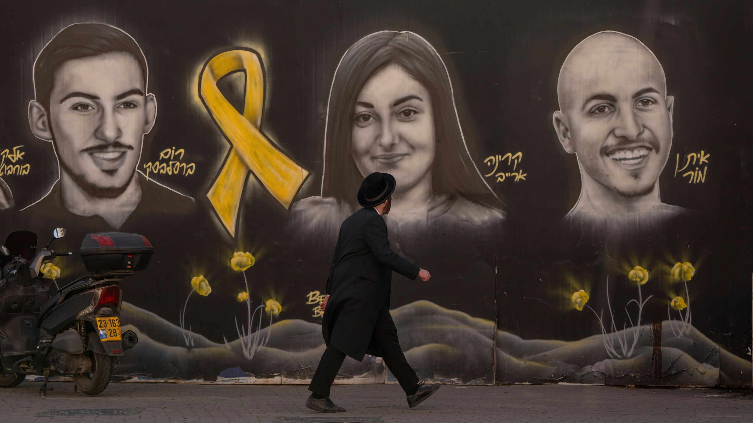 An Ultra-orthodox Jewish man walks past a graffiti that displays portraits of hostages held by Hamas in Gaza, in Jerusalem, on Monday, Jan. 13, 2025. (AP Photo/Ohad Zwigenberg)