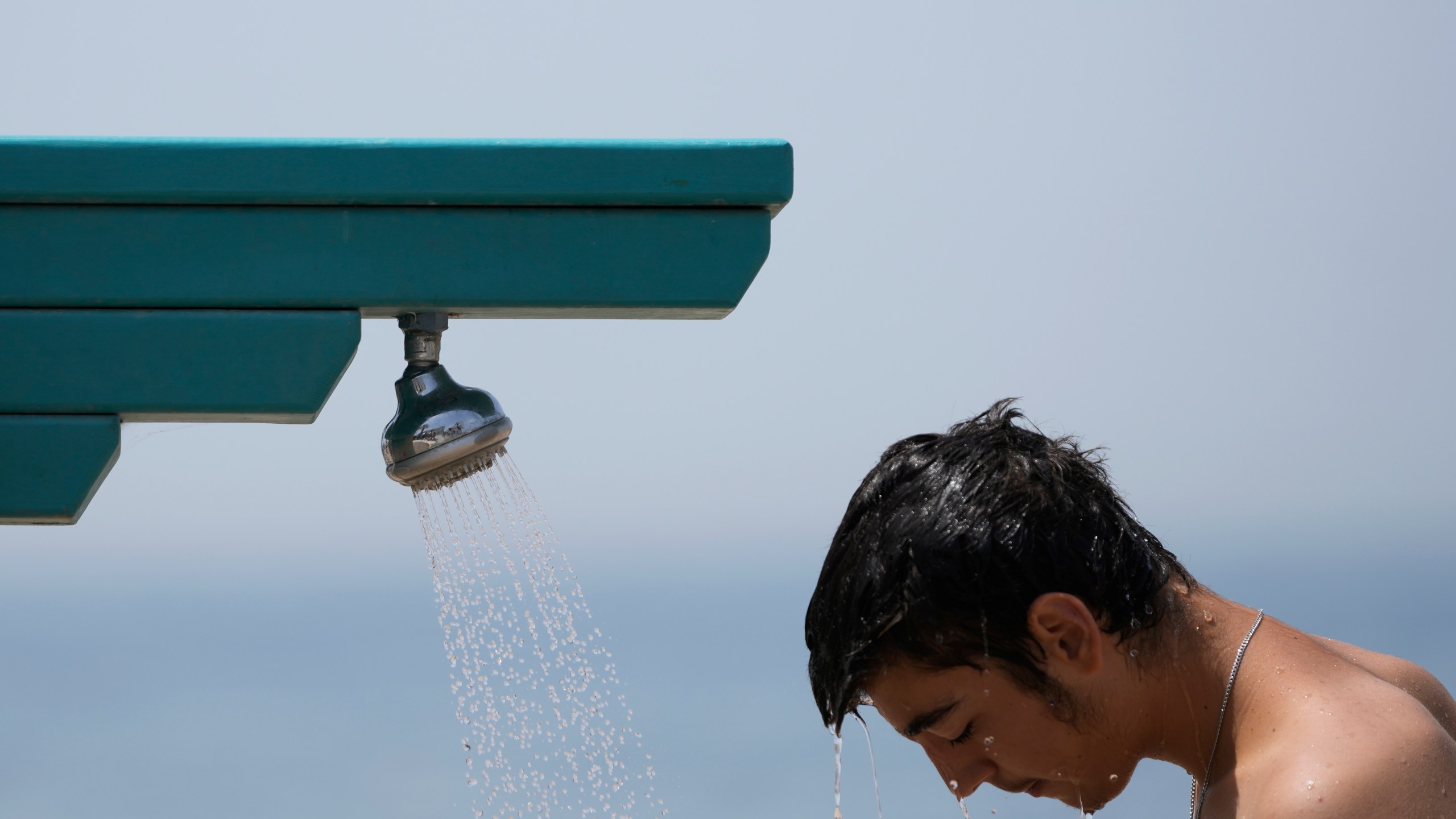 FILE - A man stands under a shower at the public beach of Paleo Faliro, in southern Athens, Greece, on June 23, 2022. (AP Photo/Thanassis Stavrakis, File)