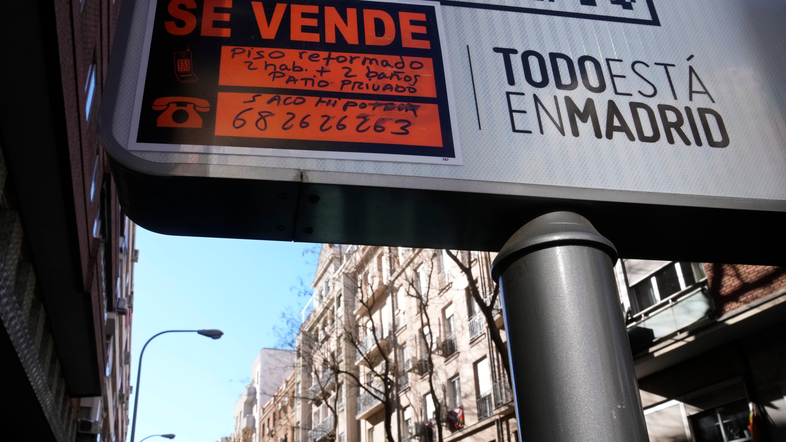 A sign advertising an apartment for sale is seen next to housing blocks in Madrid, Spain, Tuesday, Jan. 14, 2025. Sign in Spanish reads ' A renovated apartment with two rooms, two bathrooms and a private patio'. (AP Photo/Paul White)