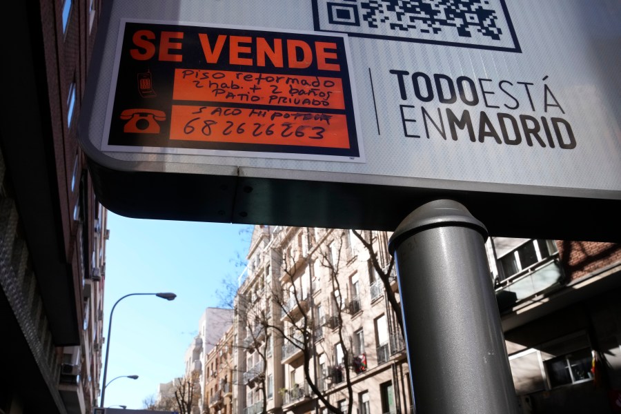 A sign advertising an apartment for sale is seen next to housing blocks in Madrid, Spain, Tuesday, Jan. 14, 2025. Sign in Spanish reads ' A renovated apartment with two rooms, two bathrooms and a private patio'. (AP Photo/Paul White)