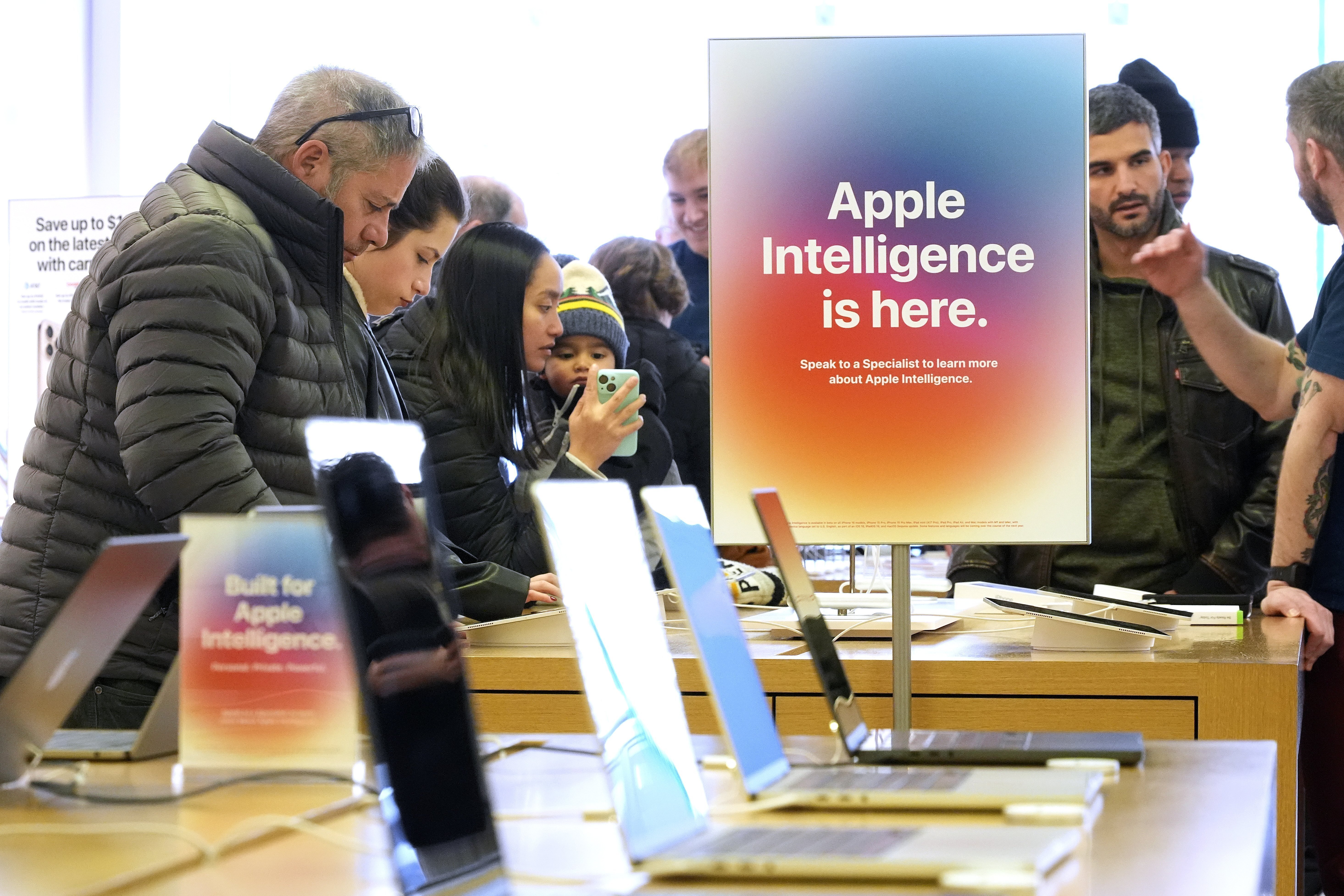 FILE - People gather around a table of iPhones at an Apple Store in Pittsburgh on Jan. 8, 2025. (AP Photo/Gene J. Puskar, File)