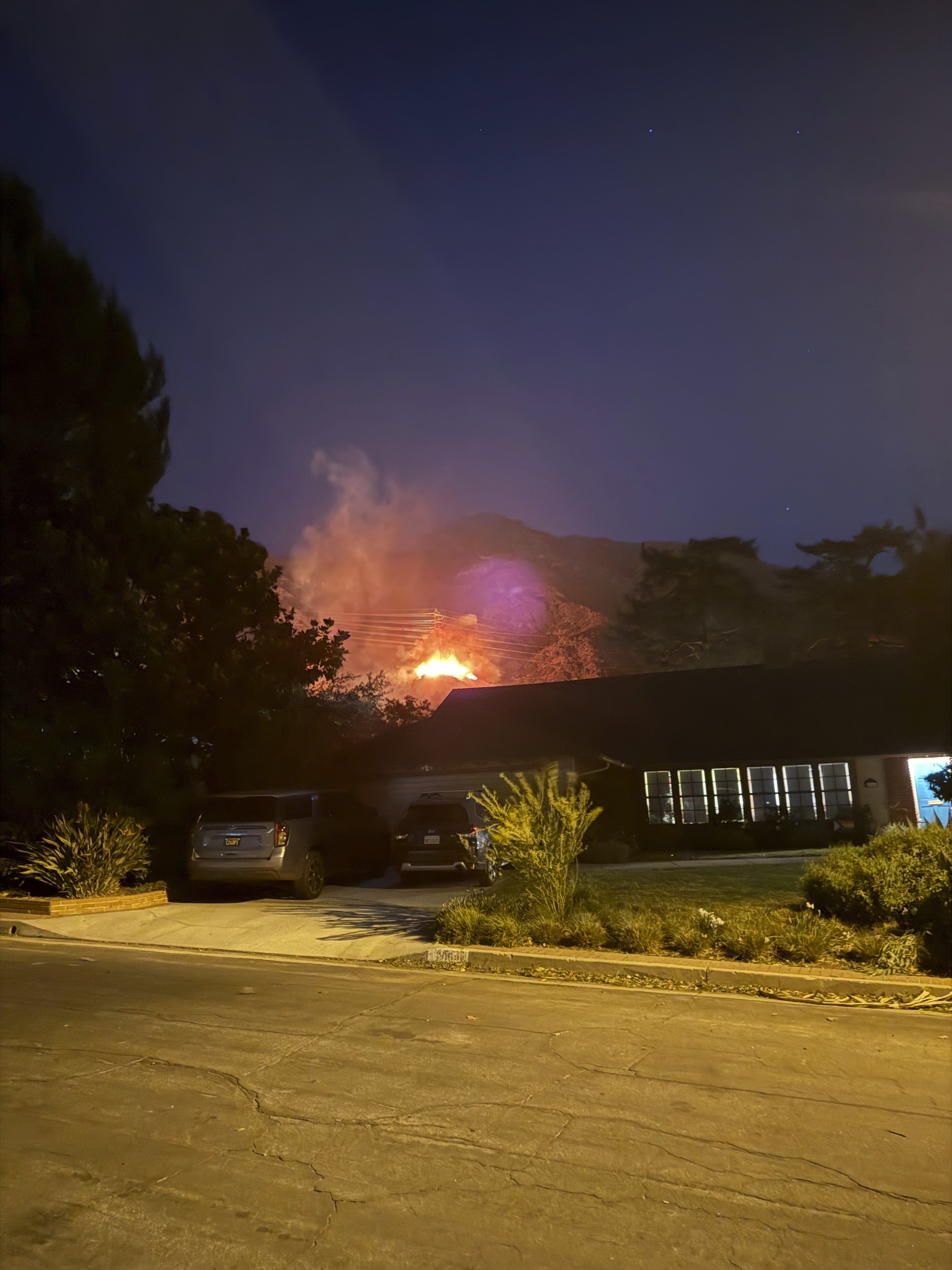 In this photo provided by Pasadena, Calif., resident Matt Logelin, flames burn beneath transmission towers owned by Southern California Edison in Eaton Canyon in the early evening of Tuesday, Jan. 7, 2025. (Matt Logelin via AP)