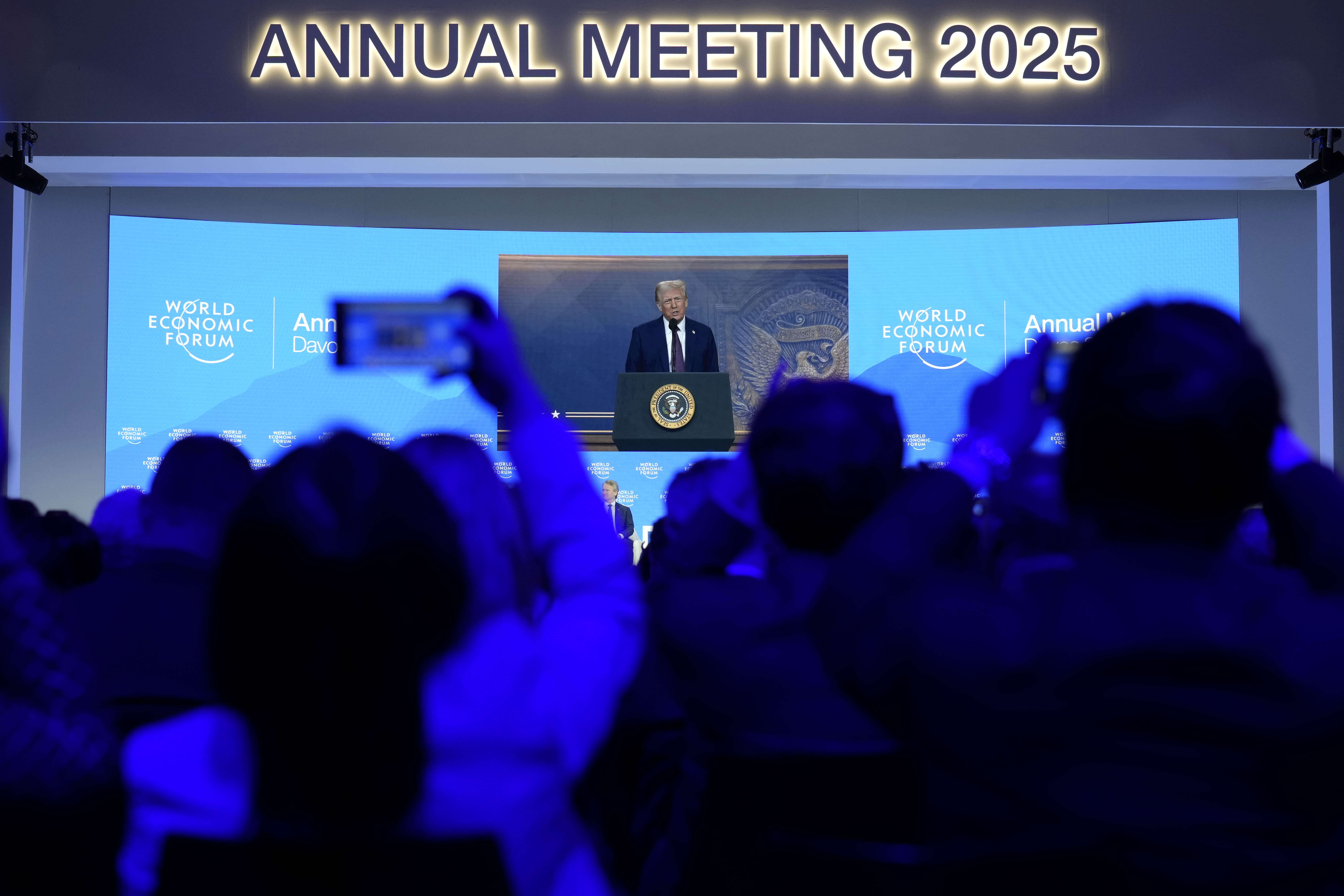 People follow a virtual speech of U.S. president Donald Trump at the Annual Meeting of World Economic Forum in Davos, Switzerland, Thursday, Jan. 23, 2025. (AP Photo/Markus Schreiber)