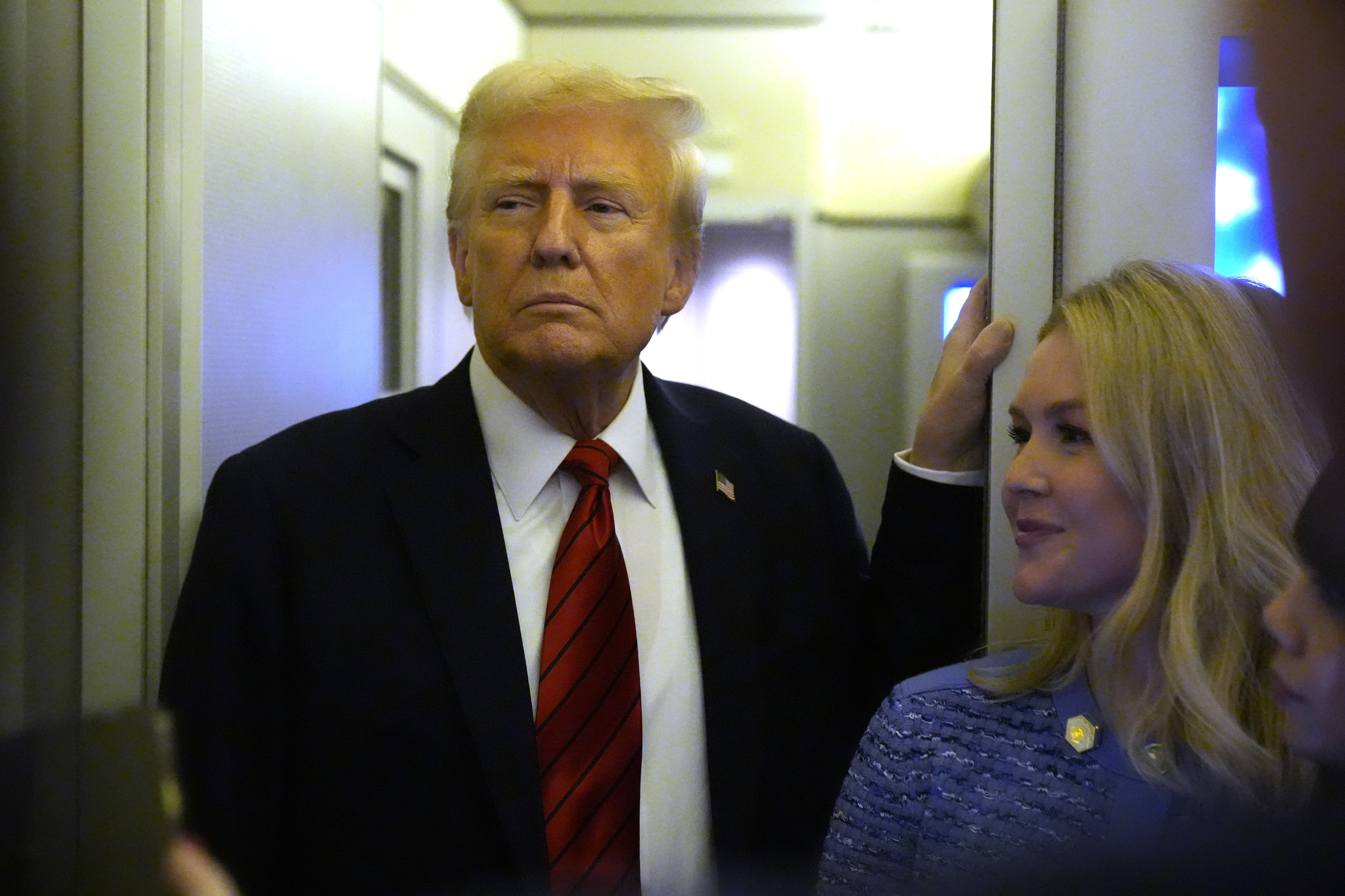 President Donald Trump speaks to reporters aboard Air Force One en route from Miami to Joint Base Andrews, Md., Monday, Jan. 27, 2025, as White House press secretary Karoline Leavitt listens. (AP Photo/Mark Schiefelbein)