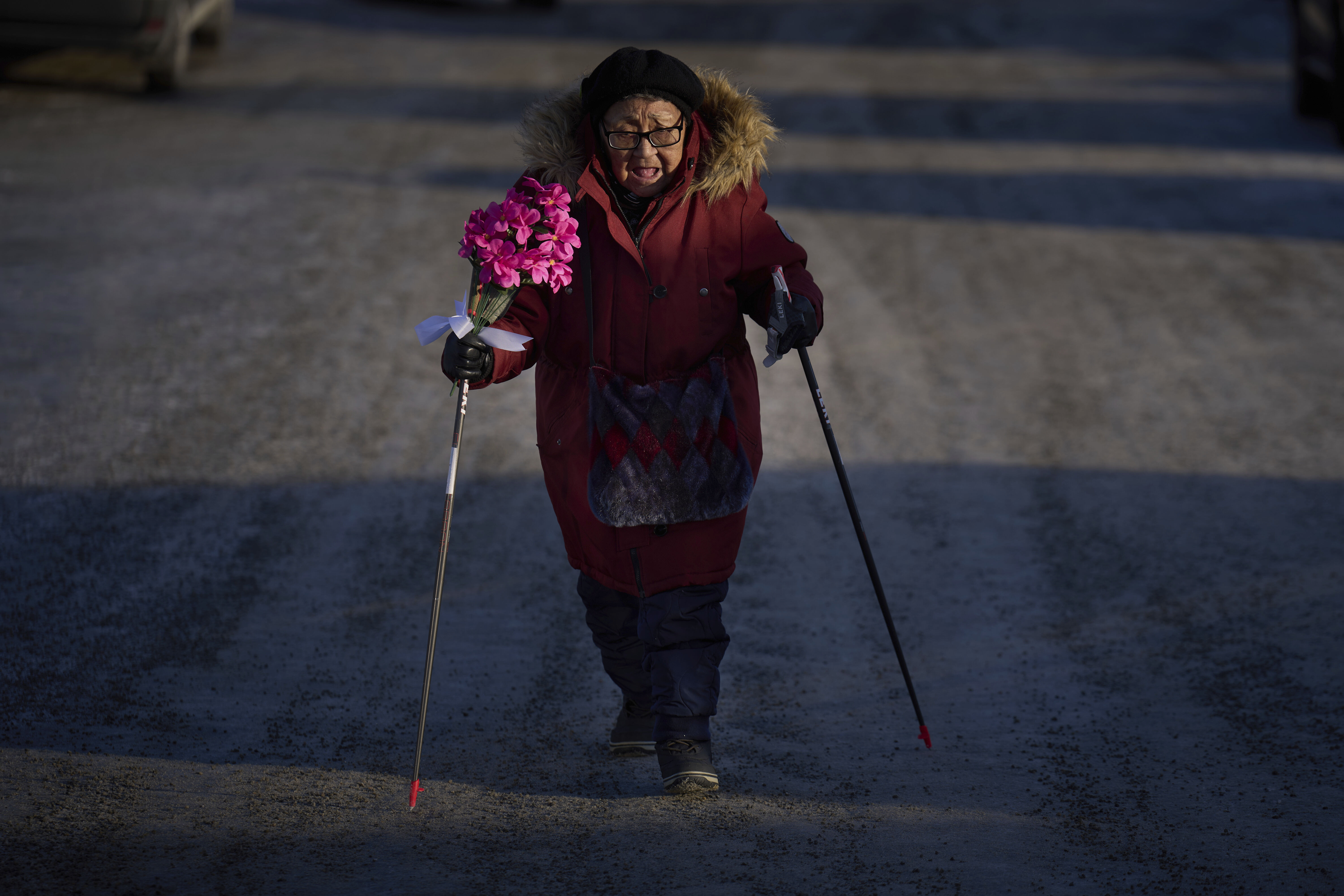 Sussane Isaksen, 79, holds a bunch of flowers as she walks through the snow-covered street to attend her friend's funeral in Nuuk, Greenland, Friday, Feb. 14, 2025. (AP Photo/Emilio Morenatti)